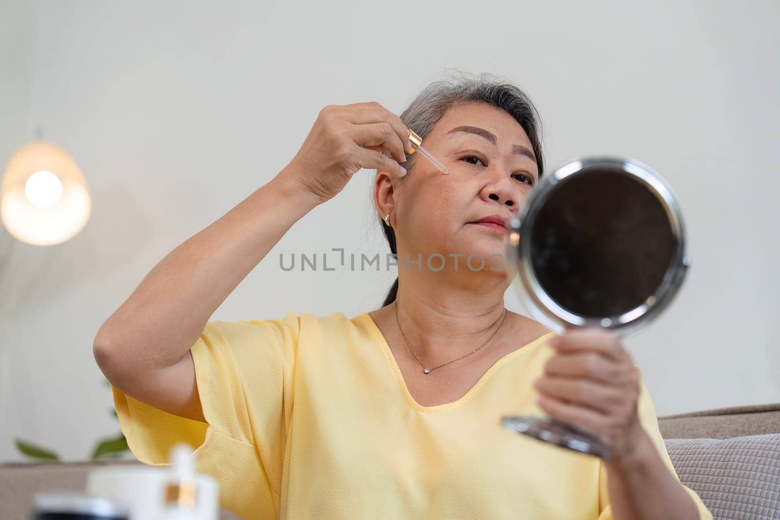 An older woman applies skincare serum while gazing into a mirror, emphasizing self-reflection and the beauty of aging gracefully.