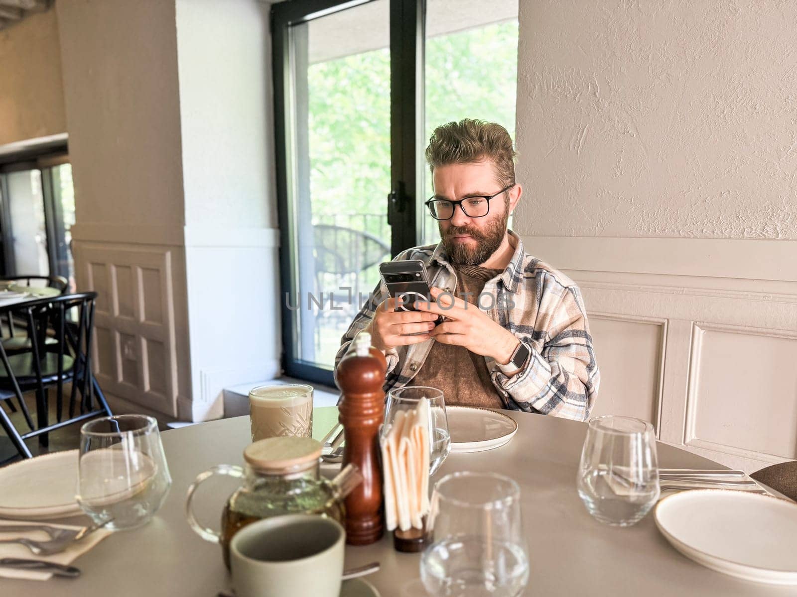 Man browsing phone at cafe table. Modern lifestyle, digital habits and casual urban dining.