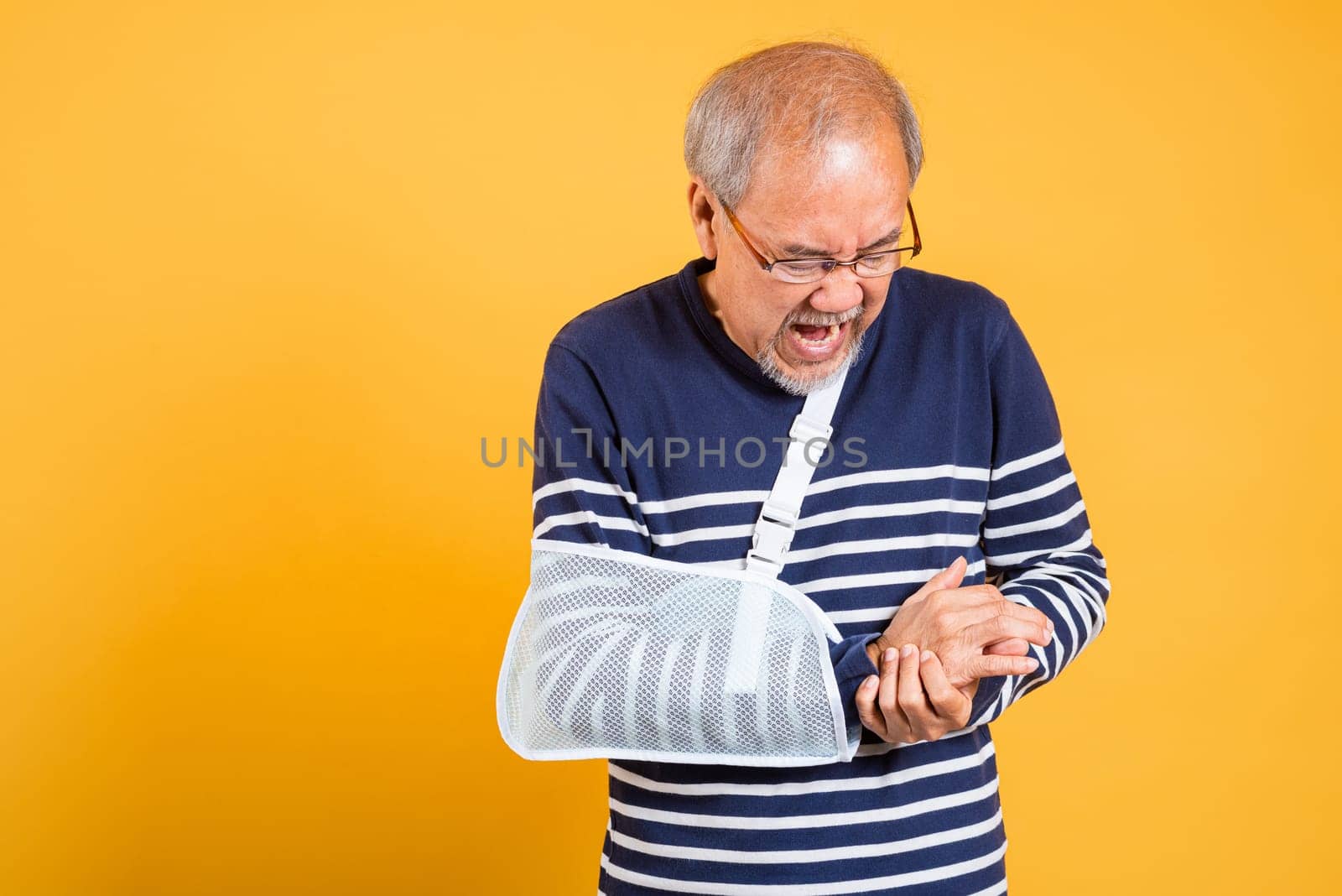 Portrait Asian old man cast on his arm painful emotions studio shot isolated yellow background, retired elderly man after accident broken arm wear arm splint for treatment accident insurance concept