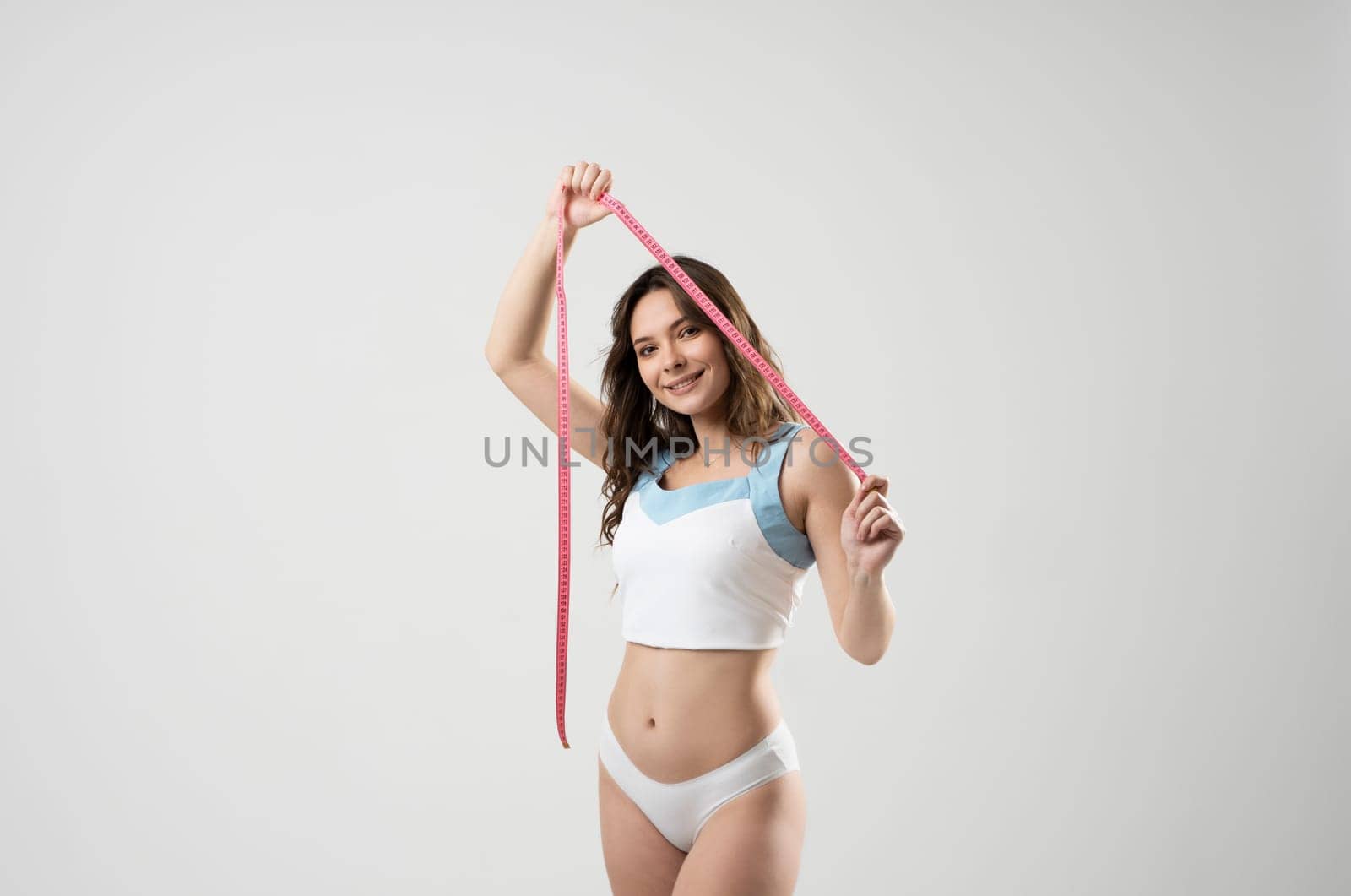Portrait of happy young woman in fitness outfit holding tape measure in hands, promoting body positivity and health tracking.