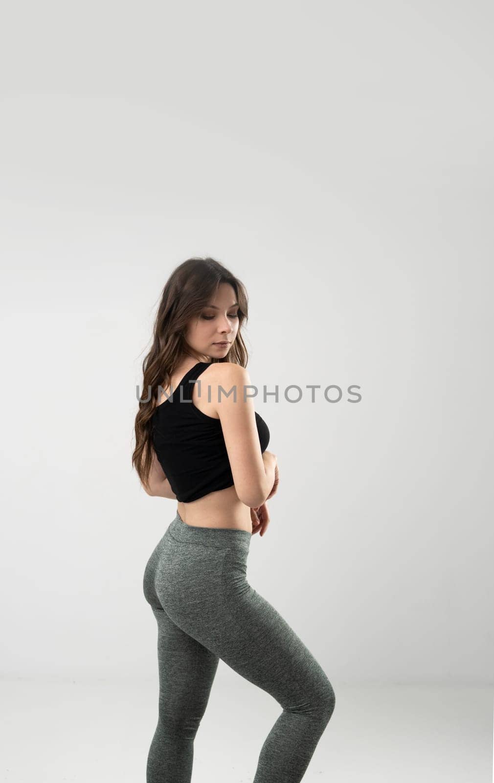 Slim woman in black top and leggings posing on white background. Fitness model, healthy lifestyle concept.