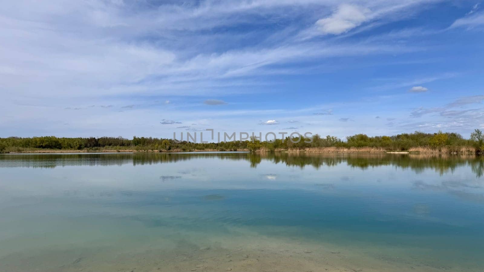 Tranquil lake landscape with clear water reflecting blue sky and lush greenery, serene nature scene ideal for relaxation and meditation, peaceful outdoor escape, nature concept, creating a serene nature scene perfect for relaxation and meditation, an ideal outdoor escape