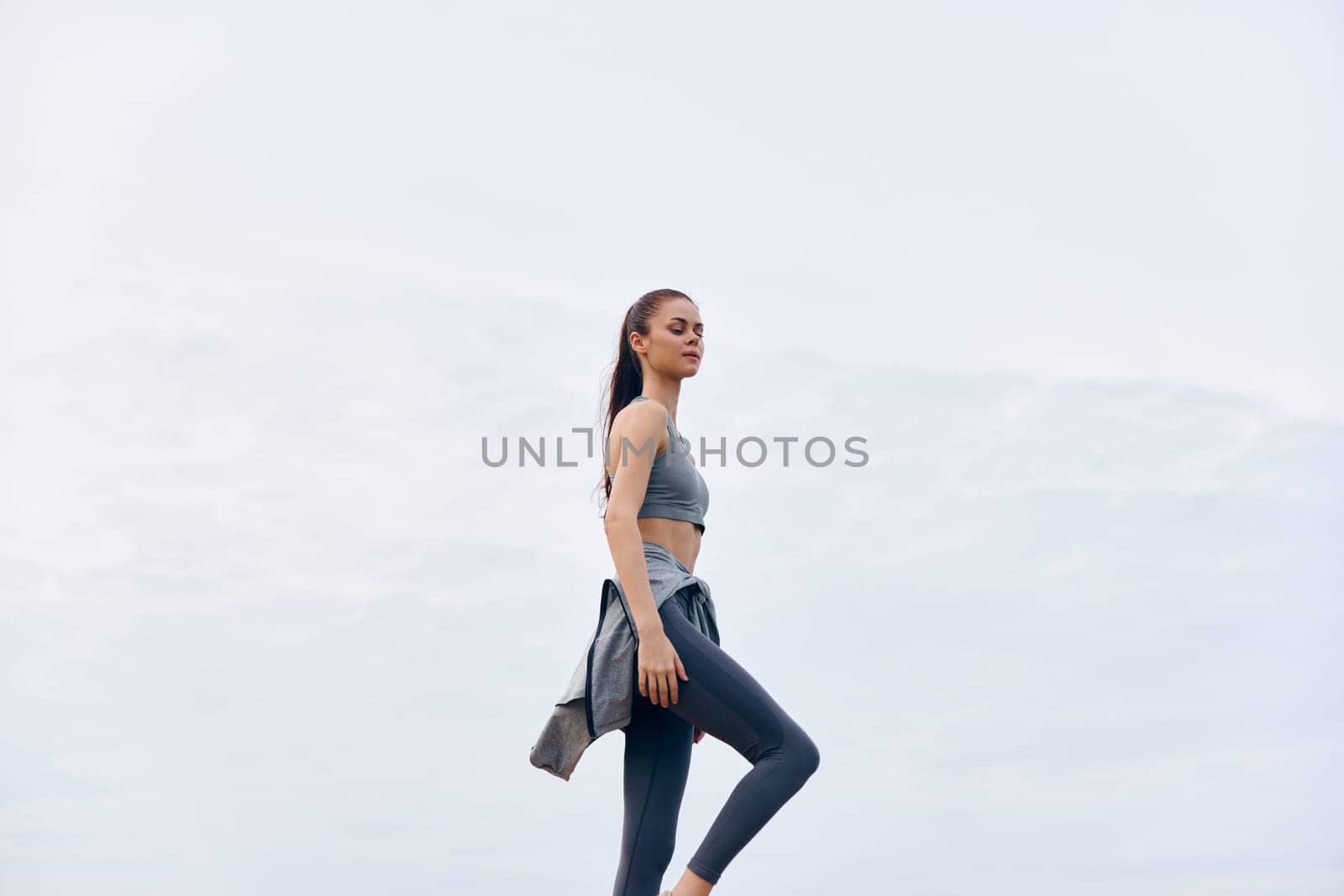 A young woman in stylish athletic wear exercises outdoors, exhibiting confidence and an active lifestyle Ideal for healthy living and fitness related themes