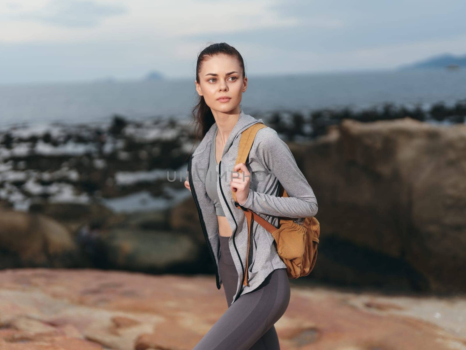 Confident female model in athletic clothing against a rocky coastal backdrop, perfect for promoting fitness, adventure, and healthy lifestyles