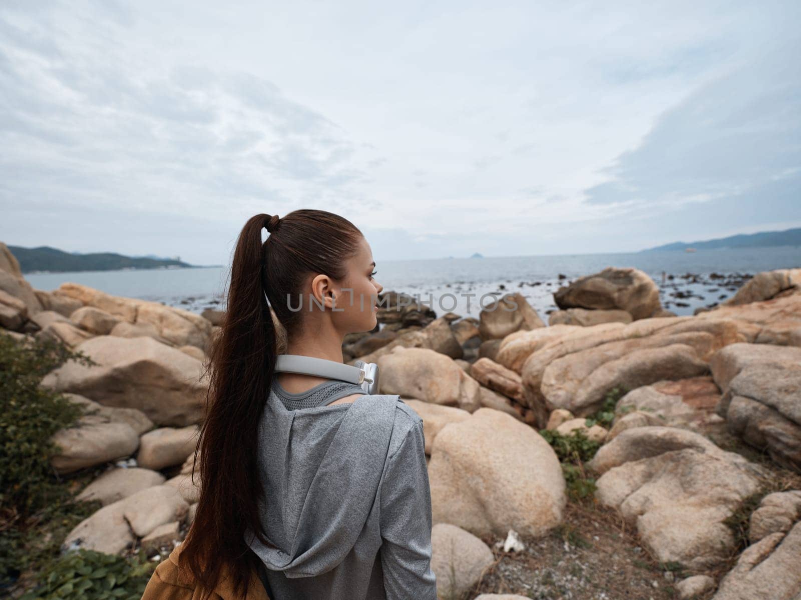 A young woman in activewear stands on a rocky shore, gazing at the ocean and contemplating nature The image promotes healthy lifestyle, mindfulness, and appreciation for natural beauty