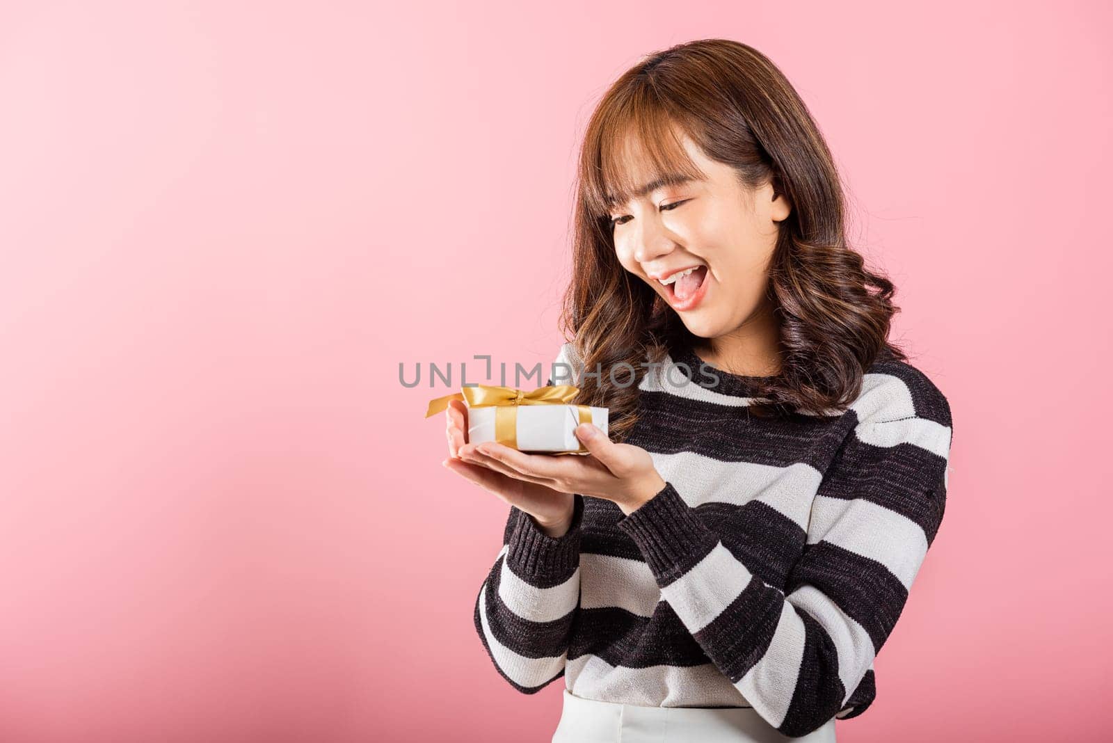 Portrait of happy beautiful Asian young woman smiling holding small gift box on hands, studio shot isolated on pink background, gift for you. Birthday, New year, Christmas, valentine day concept