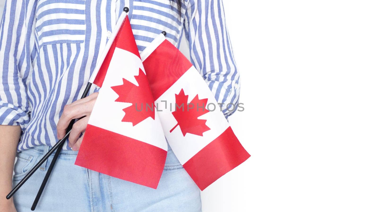 Unrecognized girl student in white blue shirt holding small Canadian flag over gray background, Canada day, holiday, vote, immigration, tax, copy space.