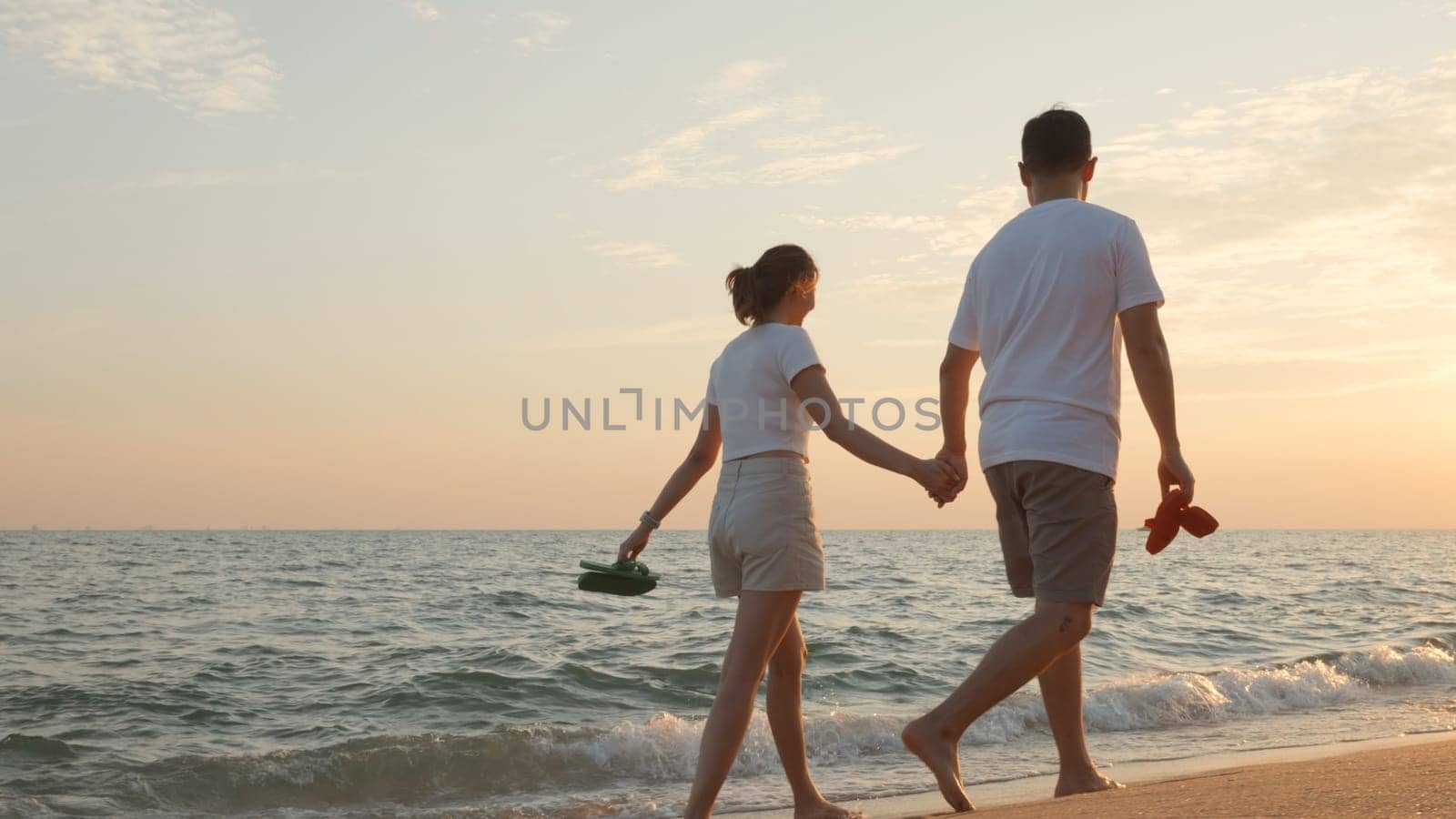Vacation loving couple walking on beach together at sunset landscape, relaxing vacation travel summer, Asian man and woman in love holding hands walks along the sandy seashore