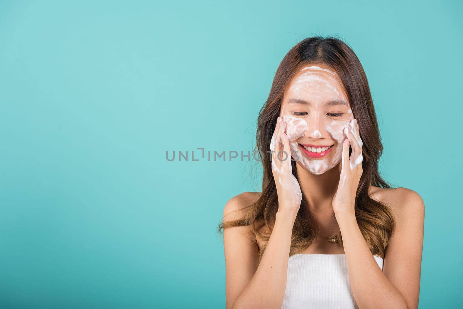Asian woman face wash exfoliate scrub soap foam with skincare cleansing, Portrait beautiful female smile applies foaming cleanser healthy skin, Studio isolated on blue background, beauty skincare