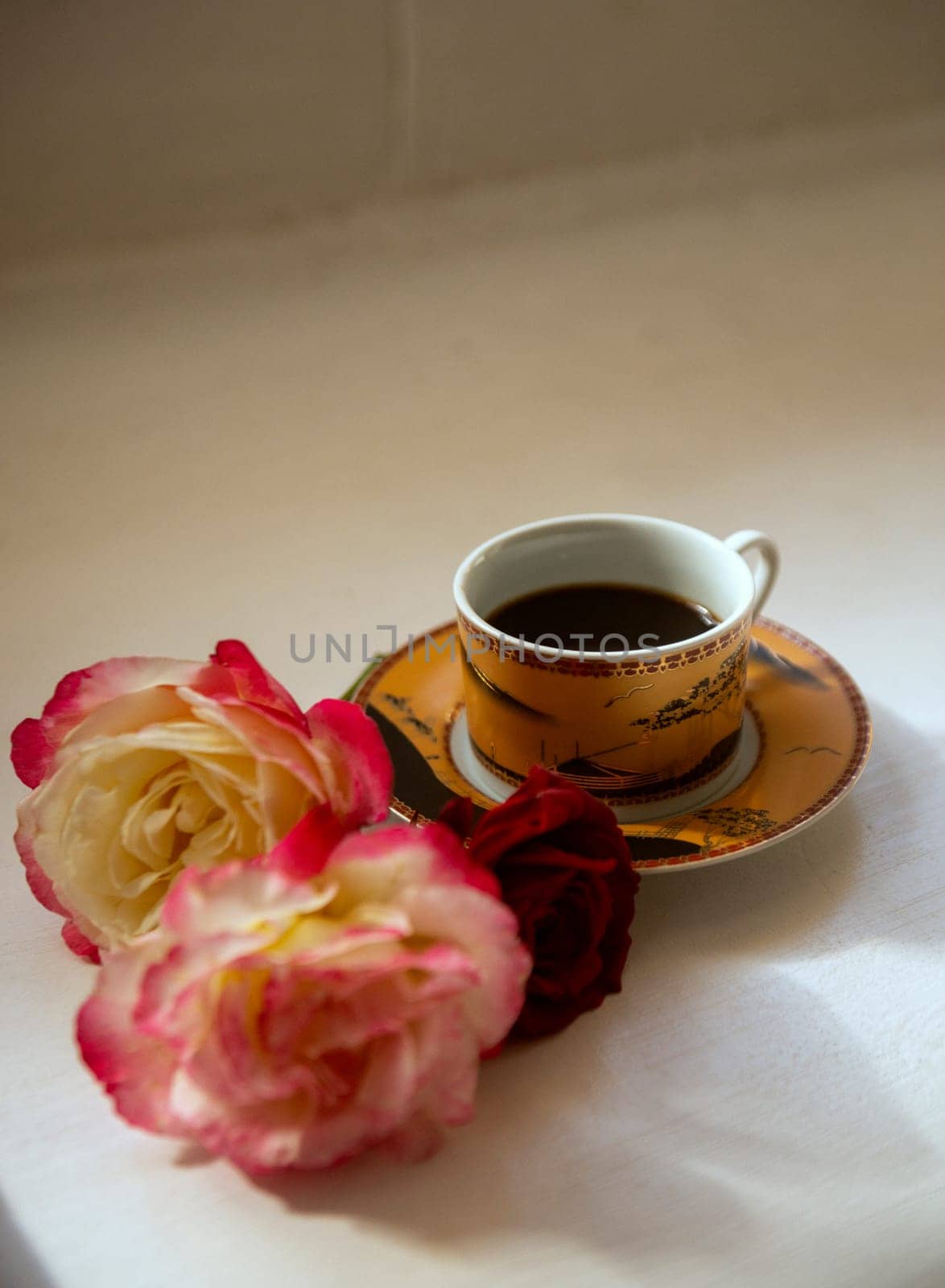 a cup of coffee on a saucer of a soft golden color and delicate pink-red rosebuds nearby. morning coffee in summer