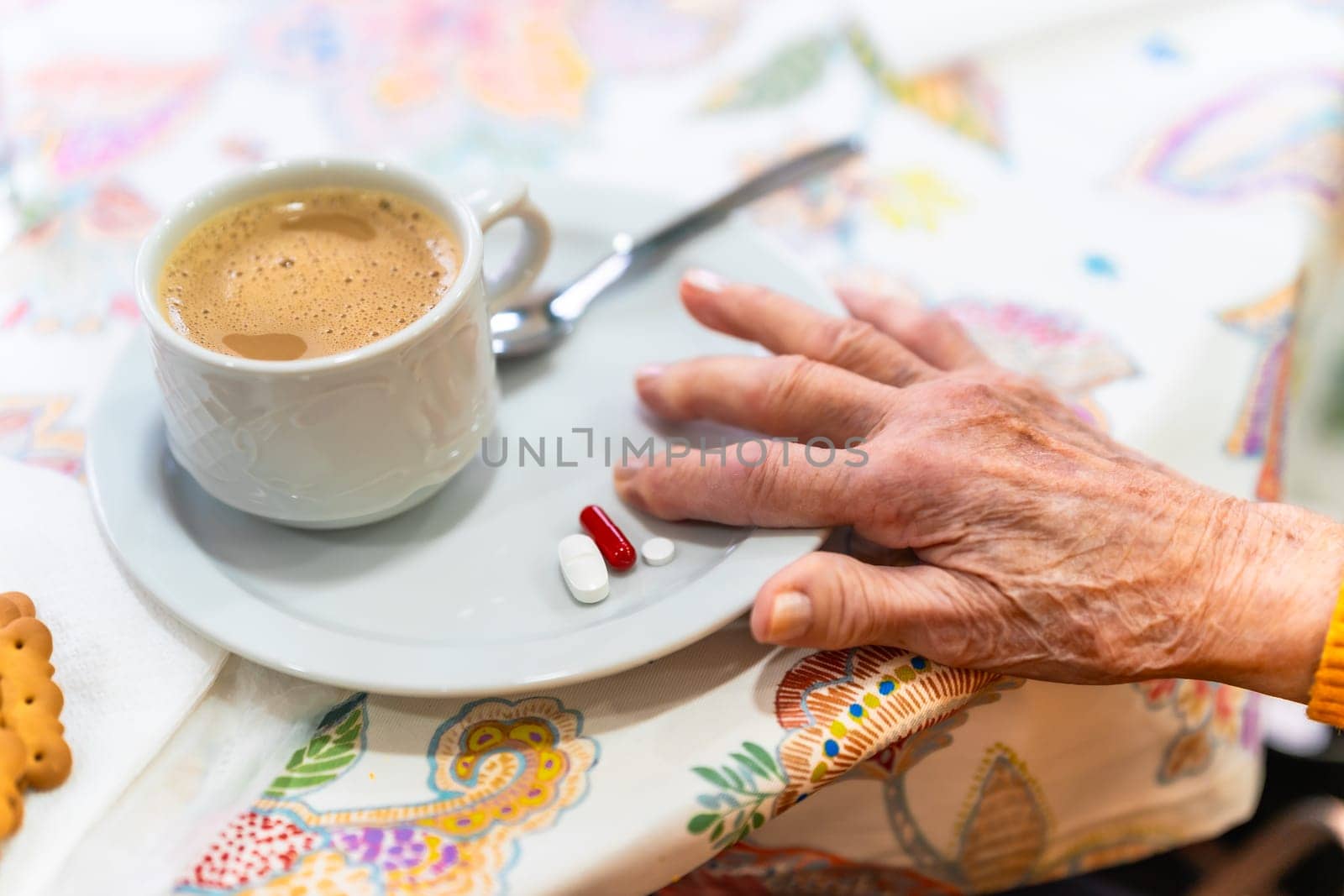 Wrinkled hand reaching for pills on saucer next to cup of coffee, highlighting medication routine in nursing home setting
