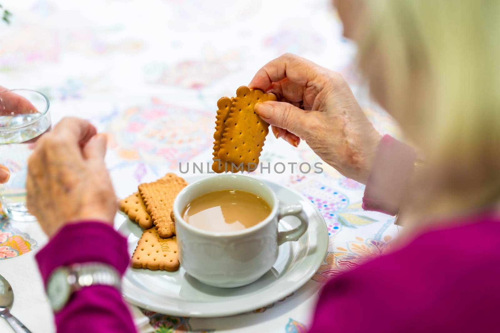 Senior woman enjoying a relaxing moment dunking biscuits into a cup of tea, representing the simple pleasures of life in a nursing home environment