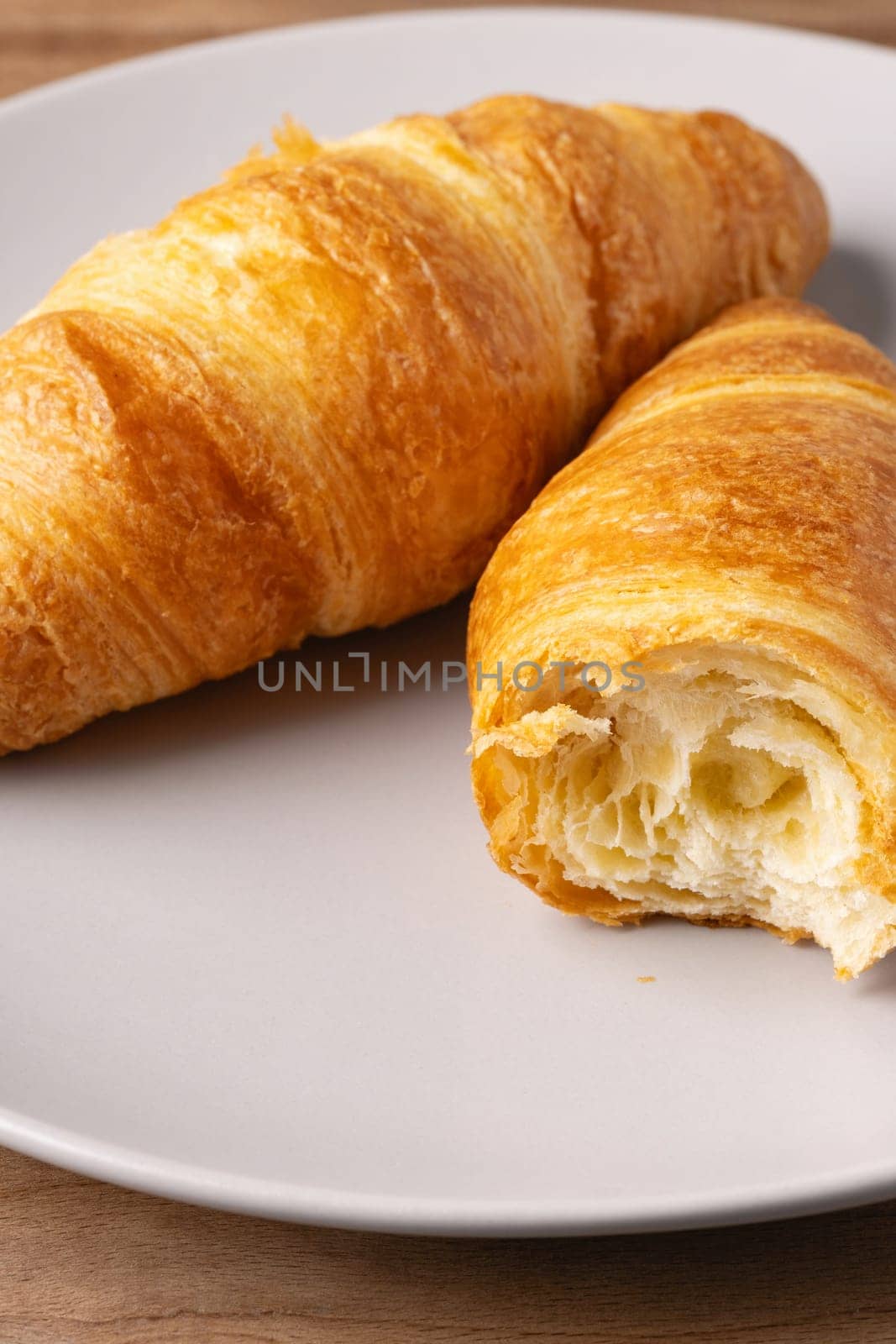 Two freshly baked croissants rest on a simple plate, displaying their flaky texture and golden brown color. The cozy kitchen setting highlights the deliciousness of this pastry.