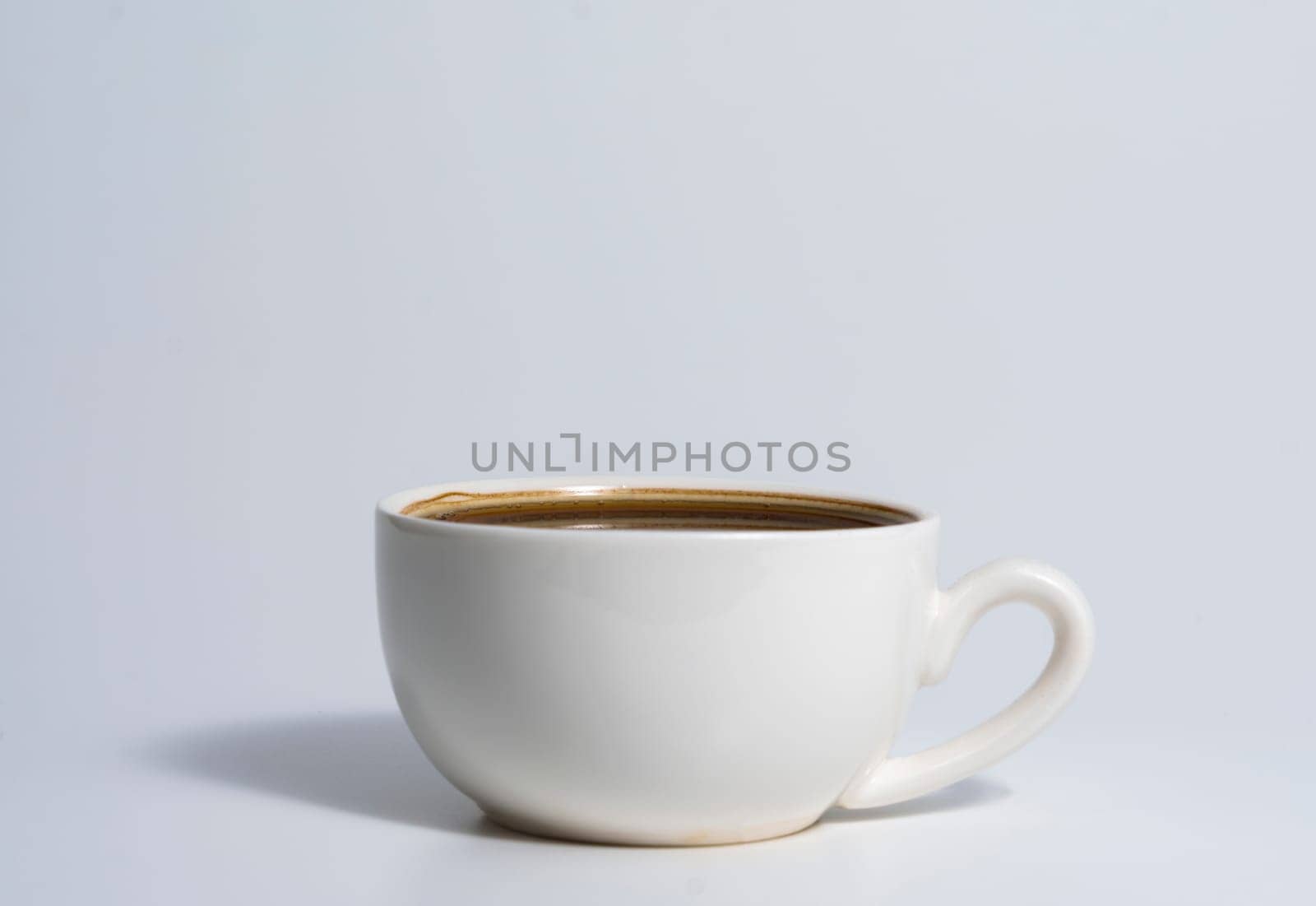Minimalistic image of a white ceramic cup filled with espresso coffee, placed on a light surface with soft shadows and a clean background.