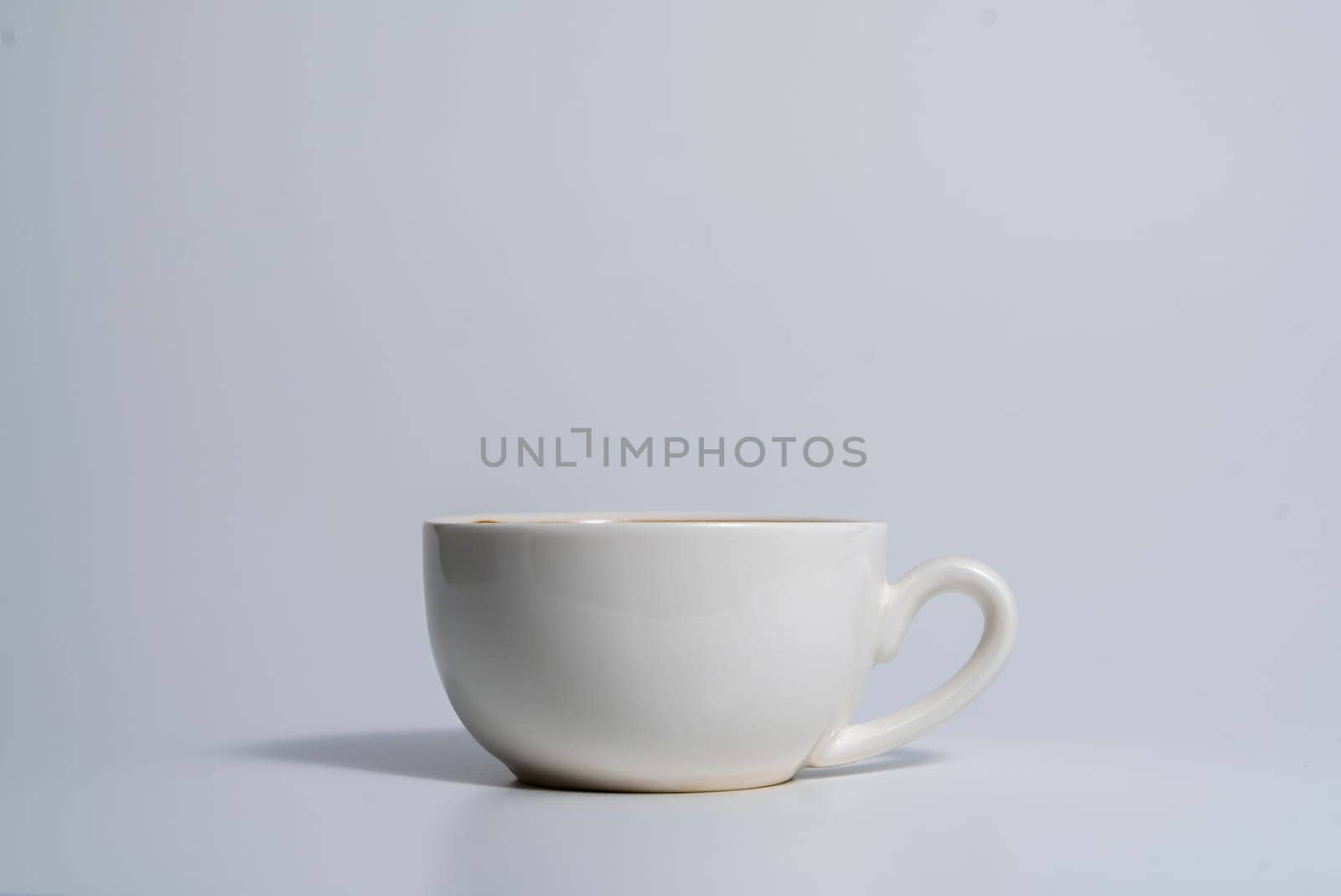 A plain white ceramic cup with handle placed on a light surface, casting a soft shadow, captured in a minimalist and clean composition.