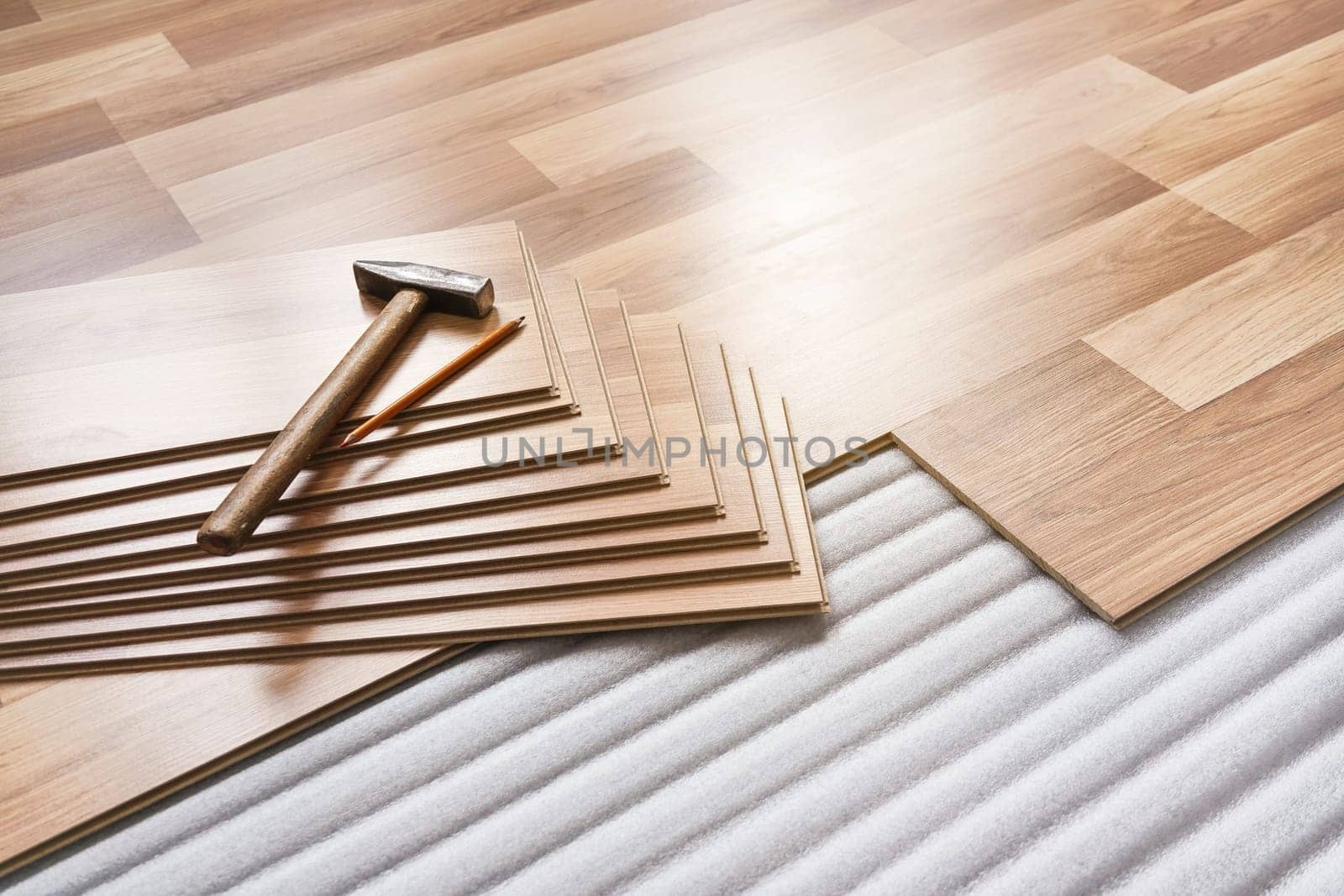 Installing laminated floor, detail on pile of wooden tiles, hammer and pencil, over white foam base layer