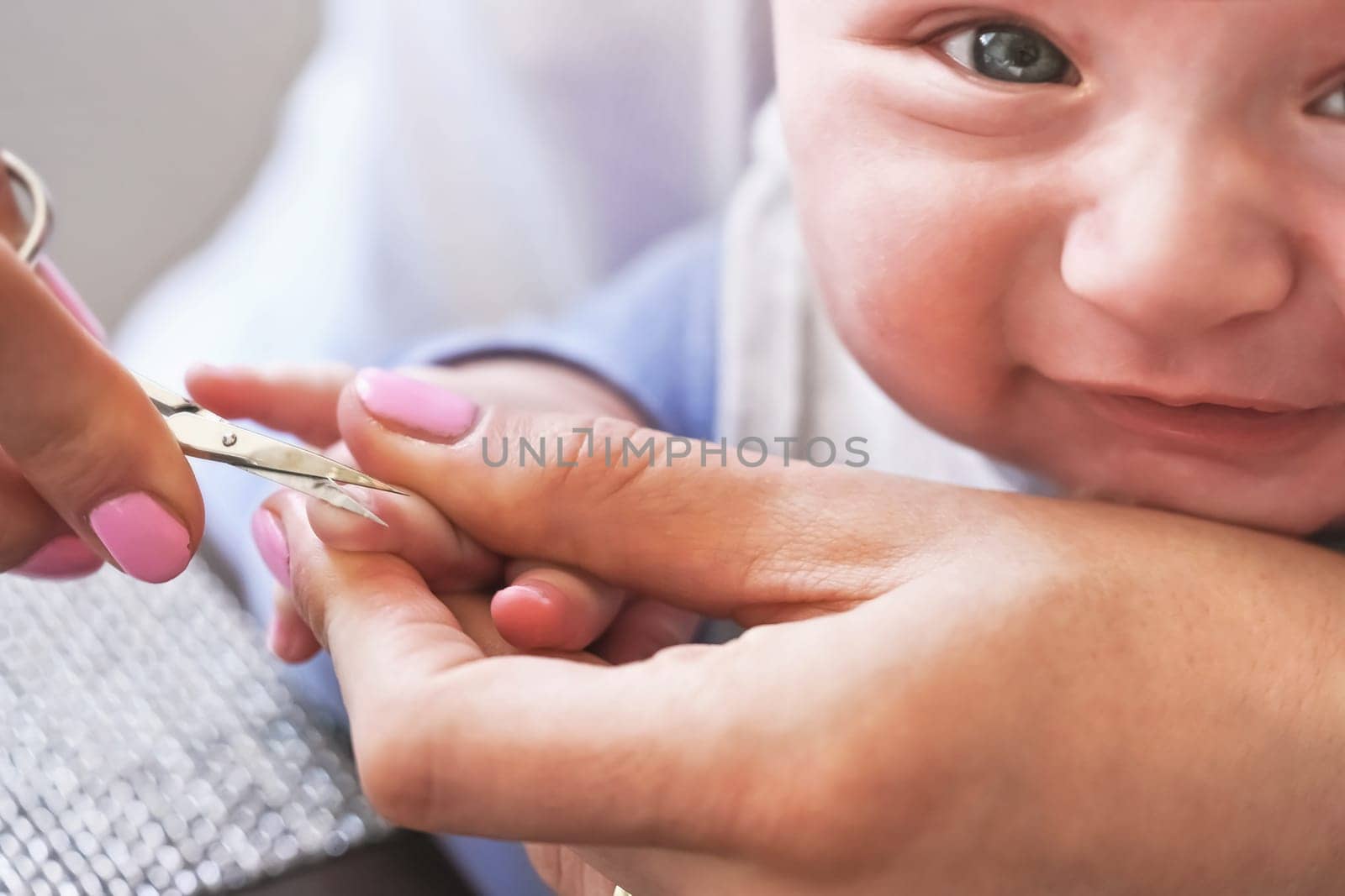 Infant baby boy having his nails cut by mother, detail on scissors and fingertips