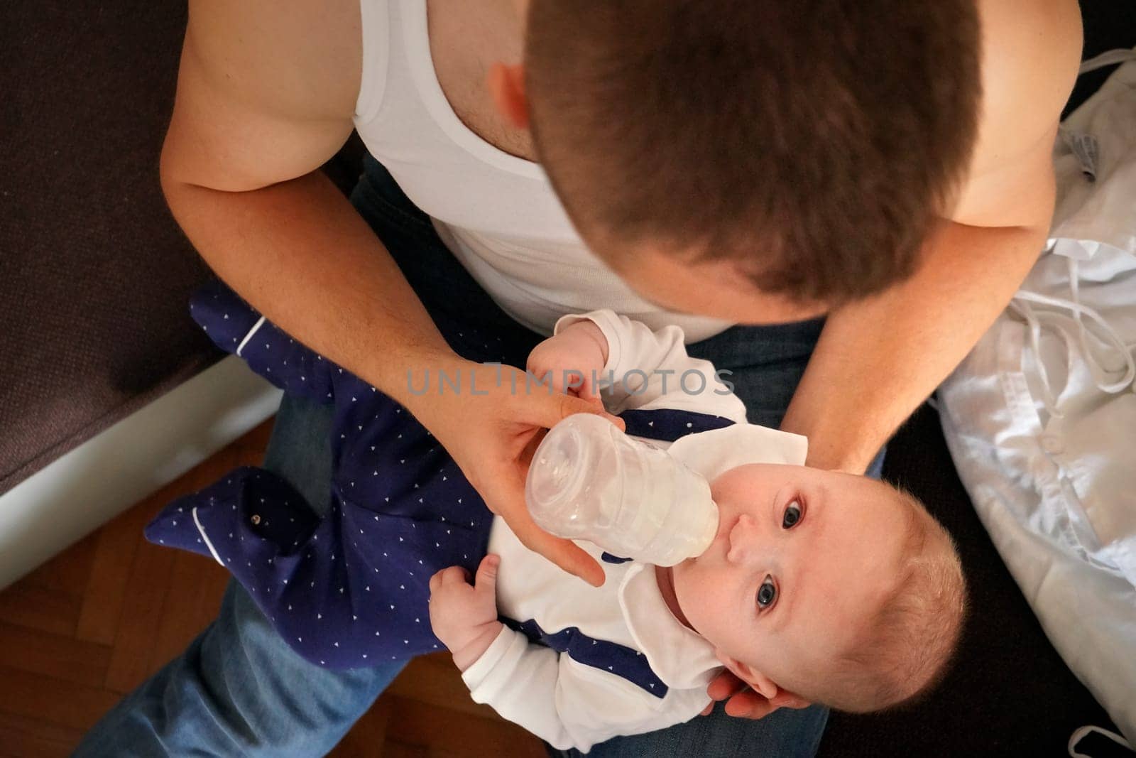 Young man feeding milk his baby boy son from bottle, view from above