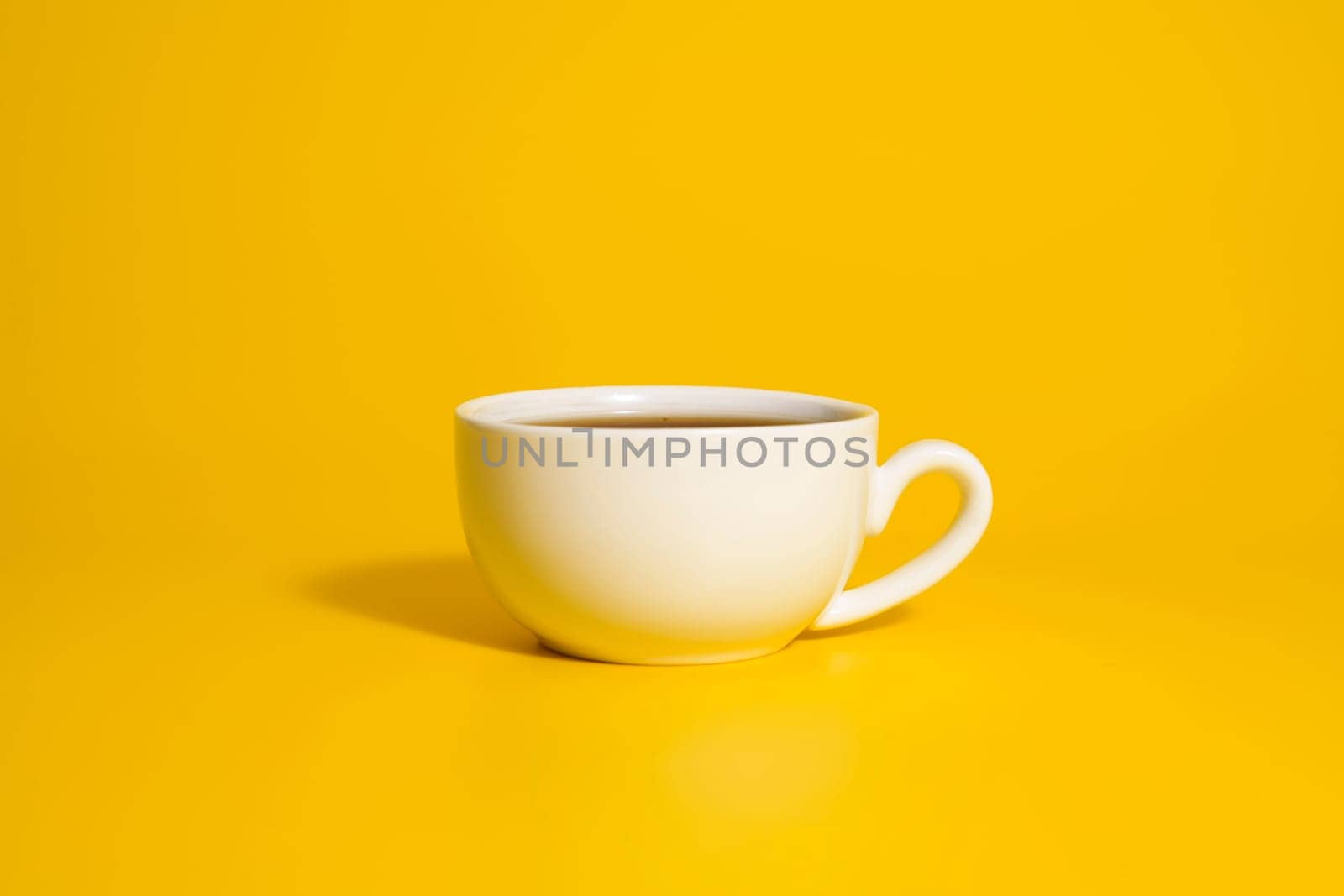 Minimalist white teacup filled with tea placed against a vivid yellow backdrop, creating strong contrast and clean modern design.