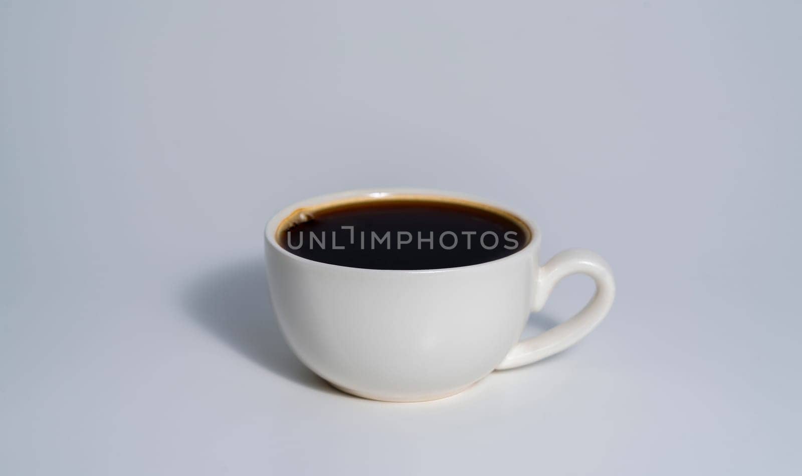 A simple white cup filled with black coffee placed against a clean light background, casting a soft shadow.