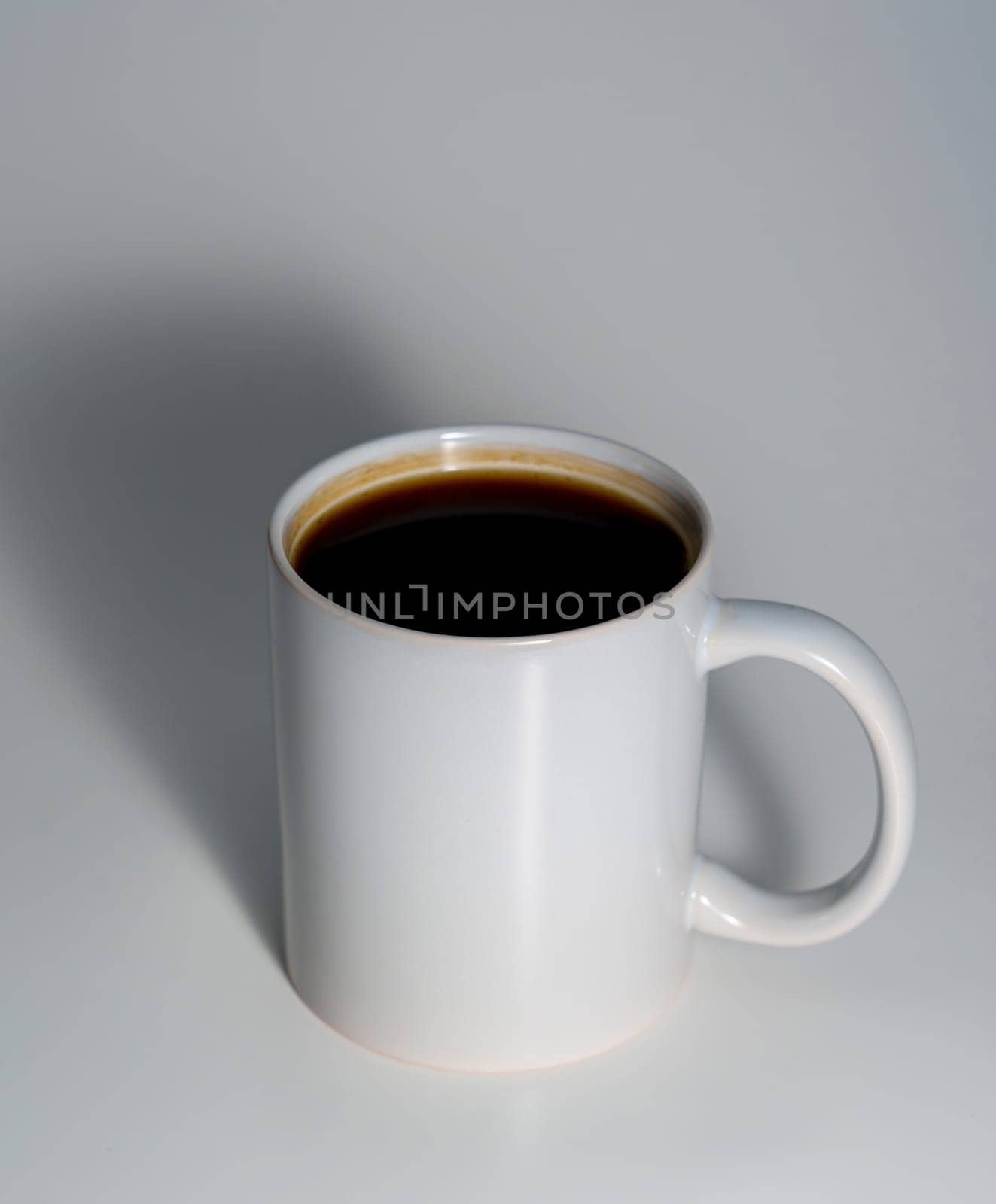 A white ceramic mug filled with black coffee, placed on a smooth light surface with a soft shadow, captured in a minimal and clean composition.