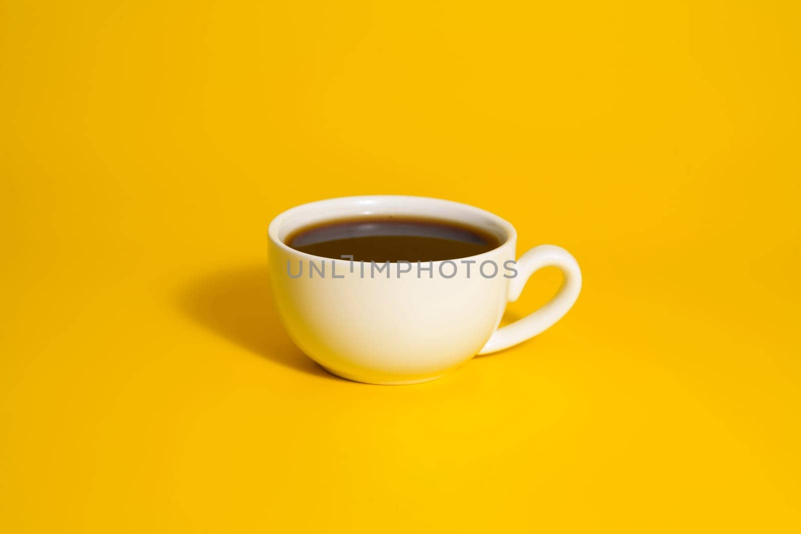 Minimalistic white cup of black coffee placed on a vibrant yellow backdrop, creating a bold and modern visual.
