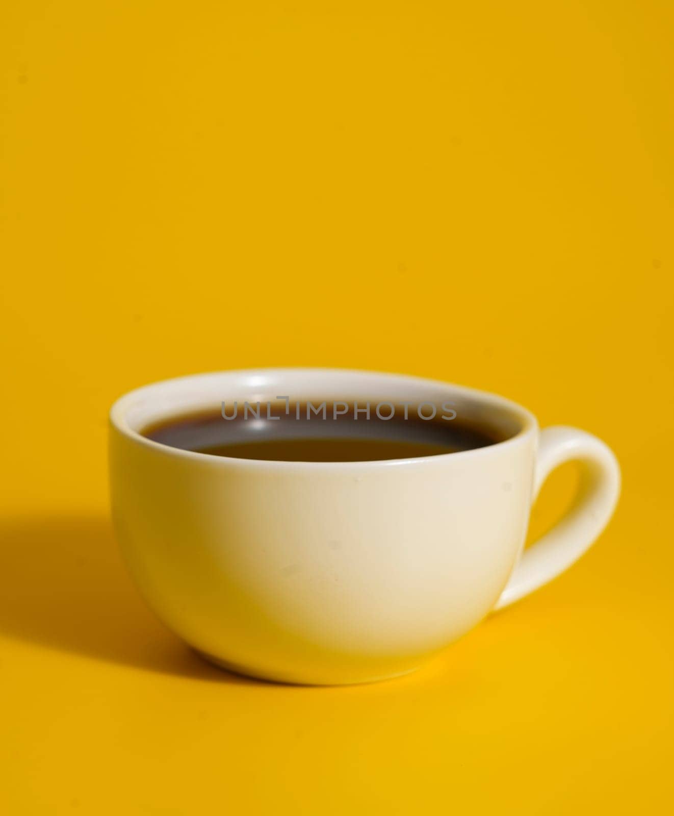 Close-up of a white ceramic cup filled with tea placed against a bright yellow background, creating a bold and clean visual contrast.