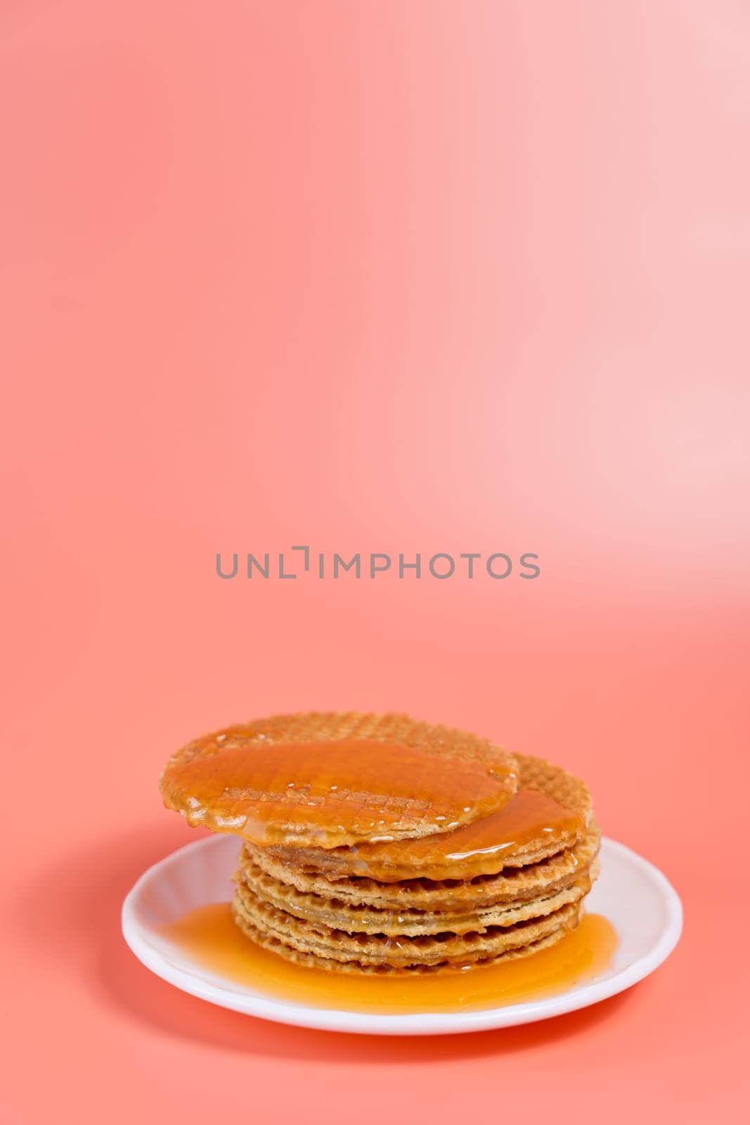 Dutch stroopwafels stacked on a white plate with warm melted caramel oozing out, set against a soft pink background.