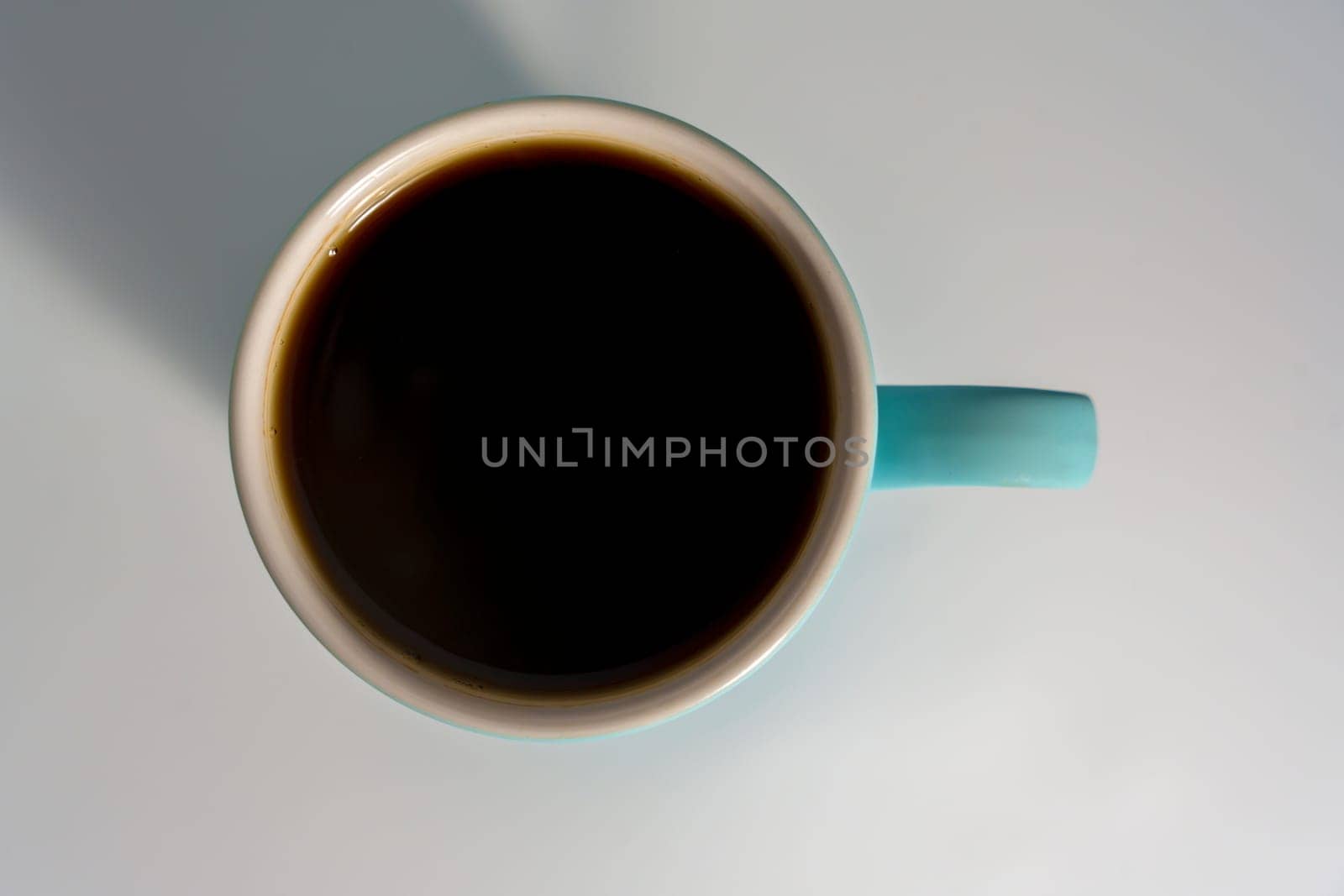 A flat lay of a filled turquoise coffee mug on a light background, with strong shadow and minimalistic composition.