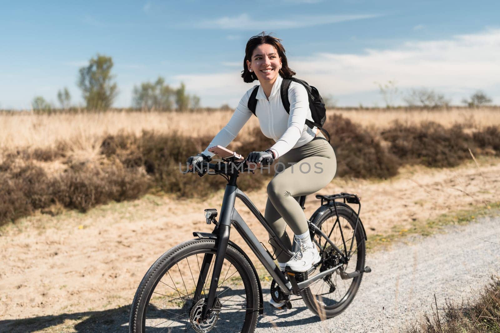 Breezy journey as a smiling woman in airy clothes pedals through a sunny day, capturing the spirit of wellness and freedom.