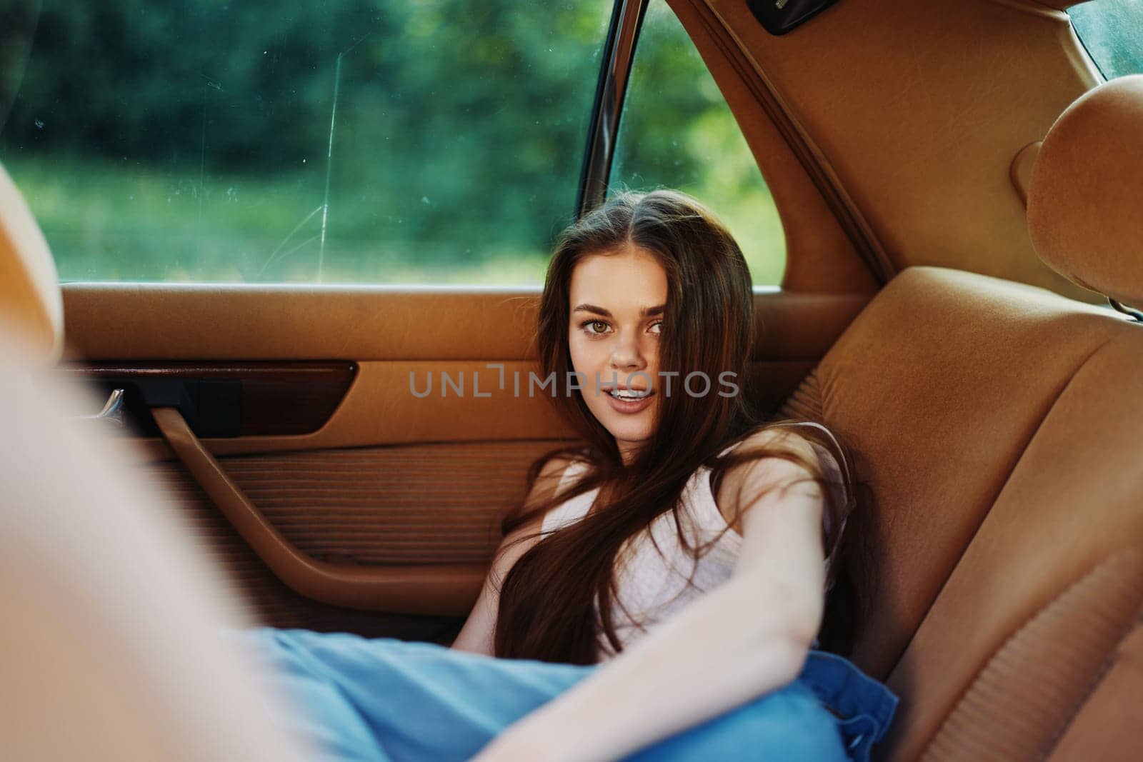 A young woman with long hair enjoying her time in a vintage car, radiating carefree emotions. The warm color palette and lush green background evoke a sunny summer day, ideal for lifestyle and travel