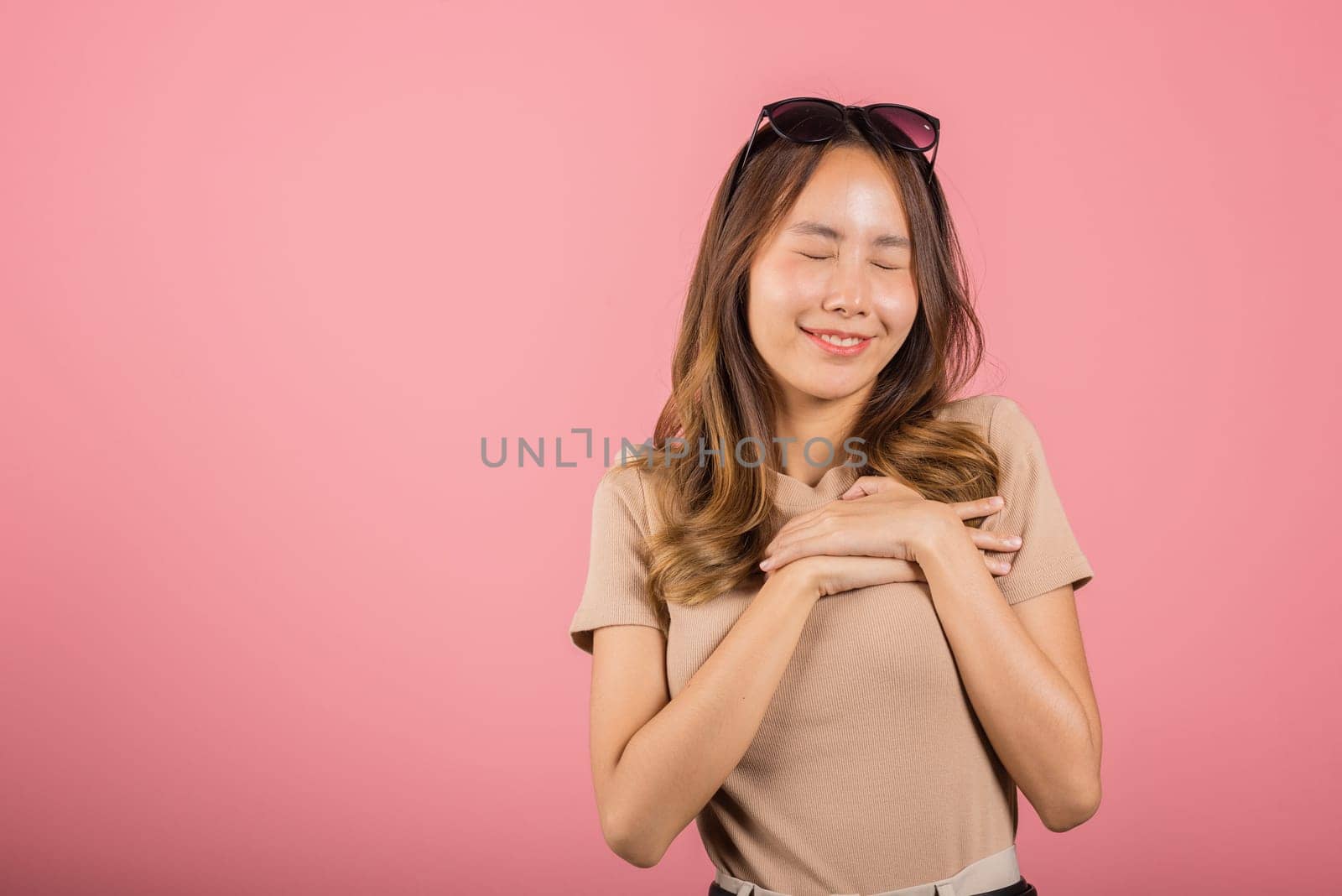 Beauty Asian young woman touching her chest for thanking in studio shot isolated on pink background, happy charming female smiling hold hands chest near heart honest with grateful gesture
