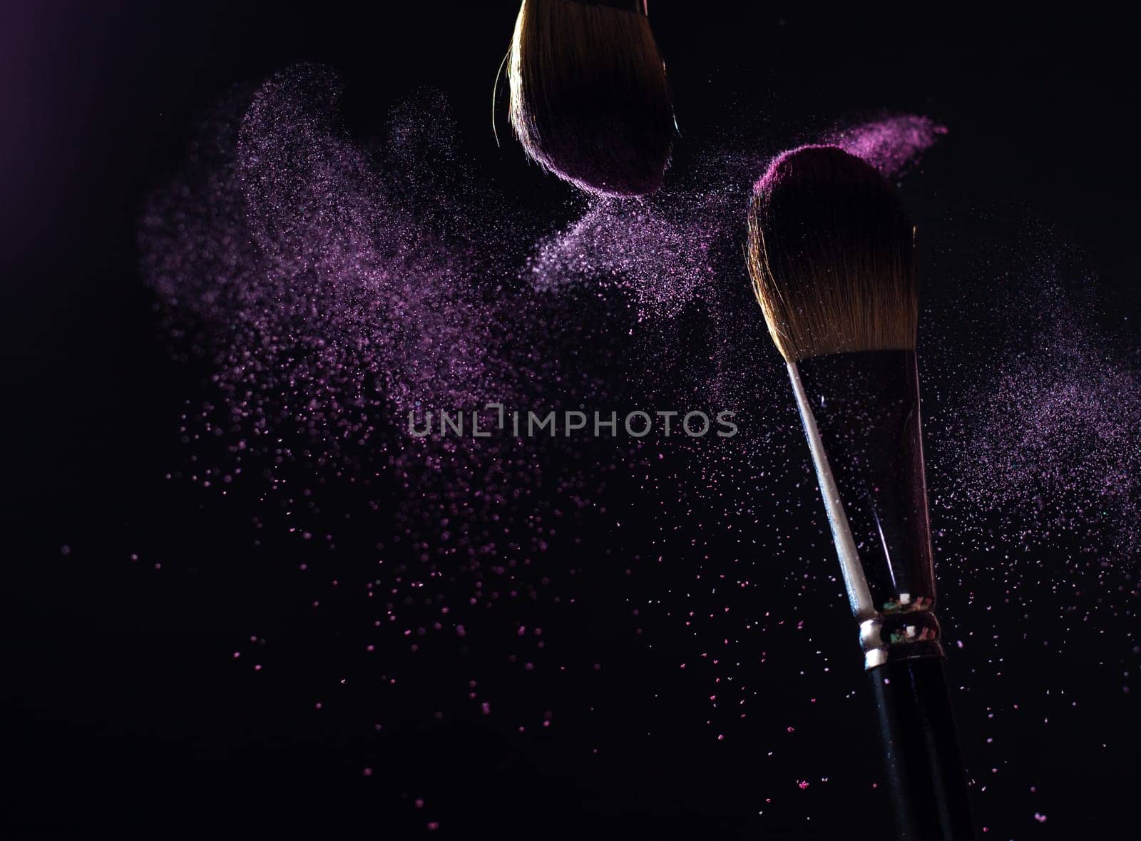 Make-up brush with pink powder explosion on black background