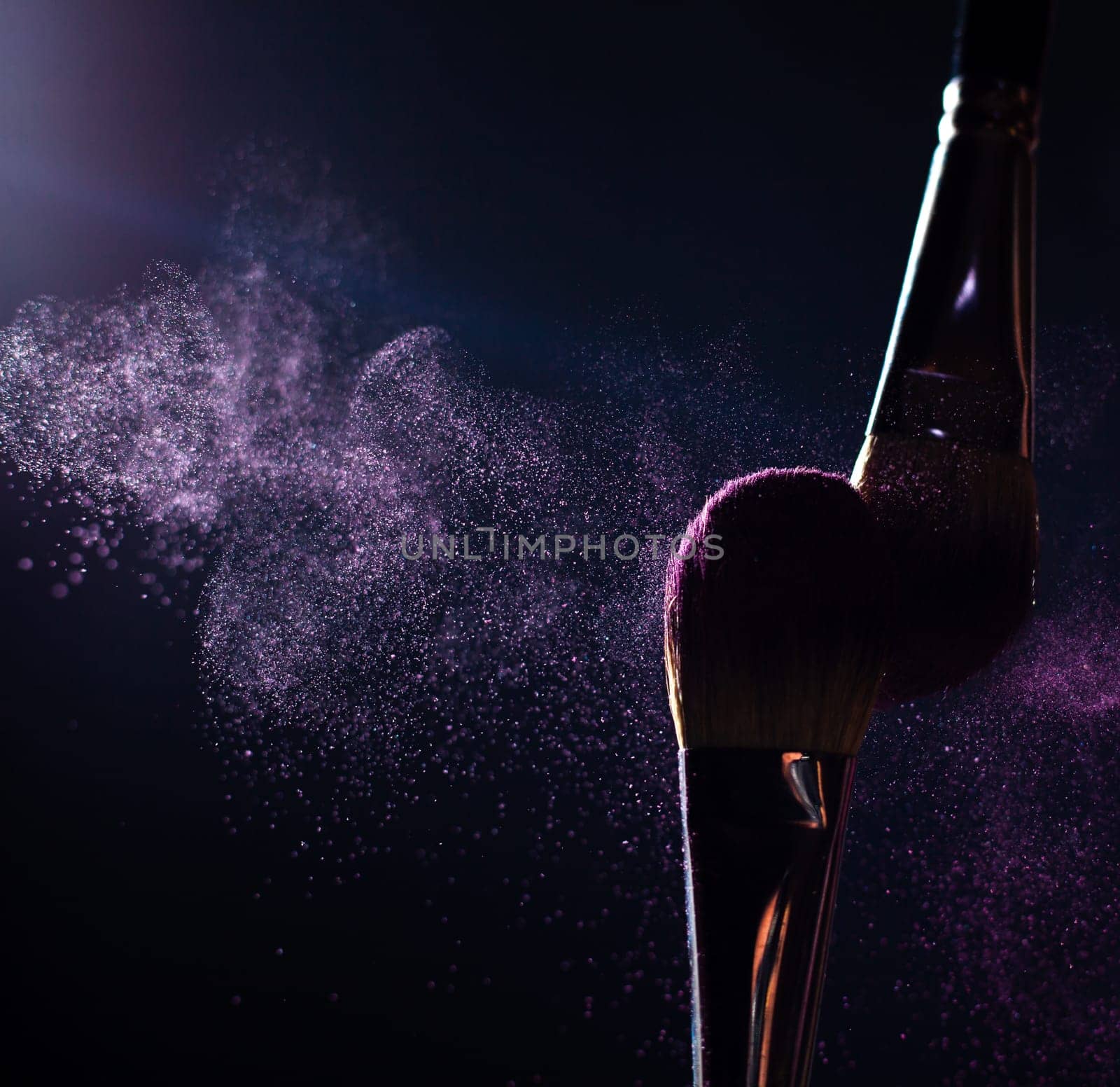 Make-up brush with pink powder explosion on black background
