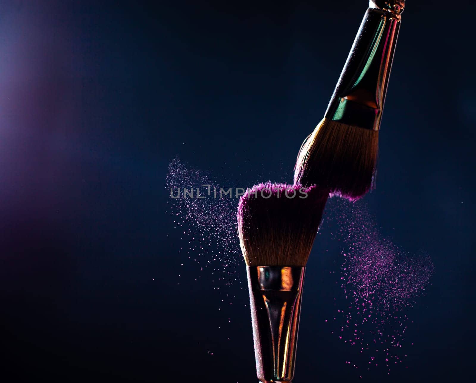 Make-up brush with pink powder explosion on black background