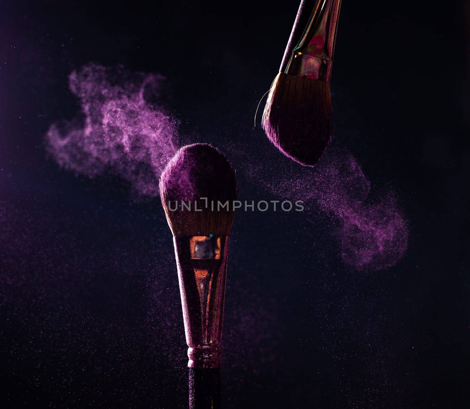 Make-up brush with pink powder explosion on black background