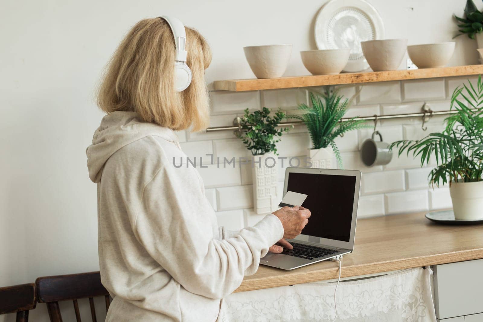 Senior woman making an online payment at home with laptop and headphones. Digital literacy and daily online activity in senior life.