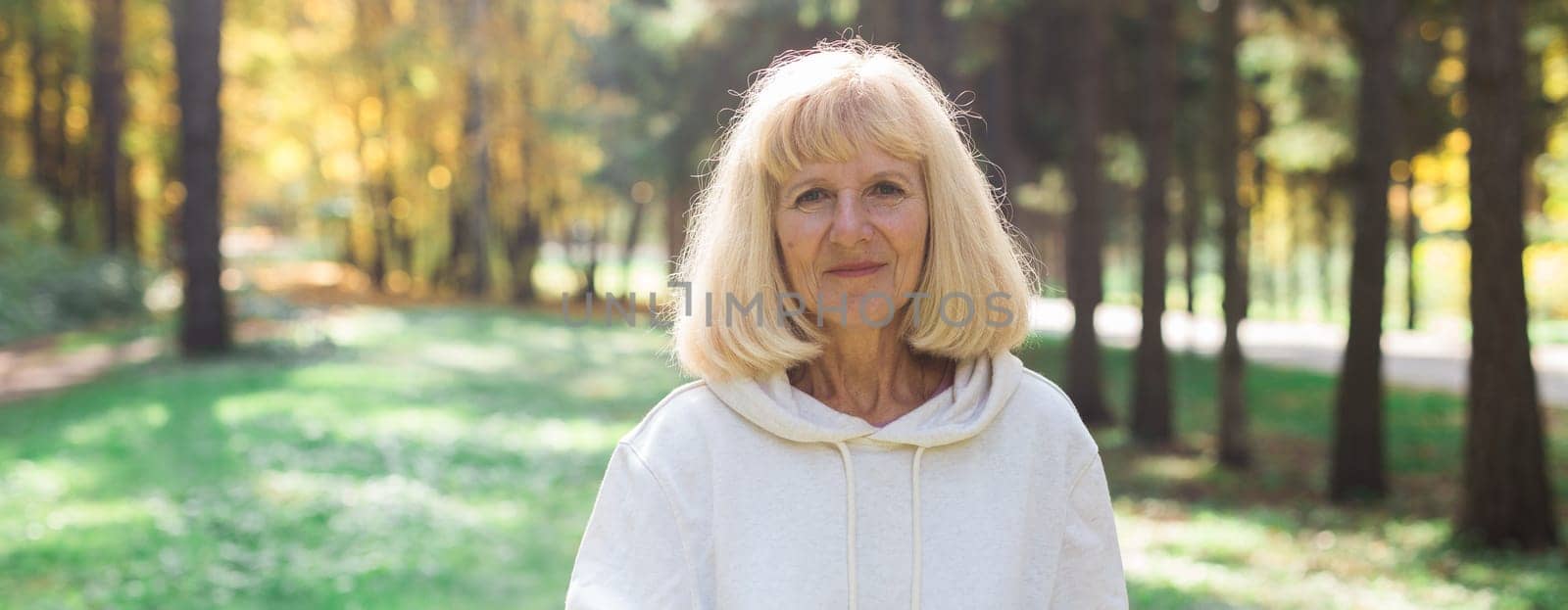Banner mature woman enjoying a sunny walk in autumn forest, copy space. Mindfulness, relaxation and healthy outdoor lifestyle for seniors.