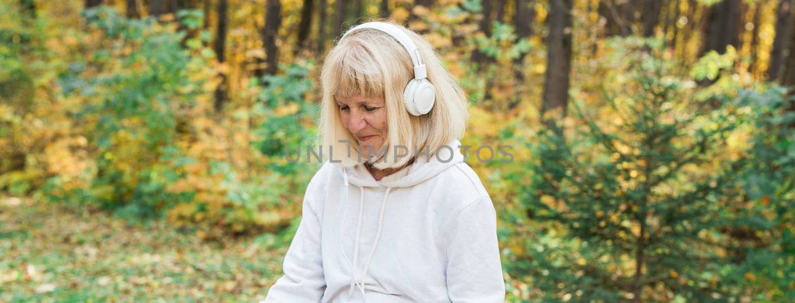 A senior woman enjoying music in the autumn forest. Relaxation, happiness, mindfulness and connection with nature during active aging.