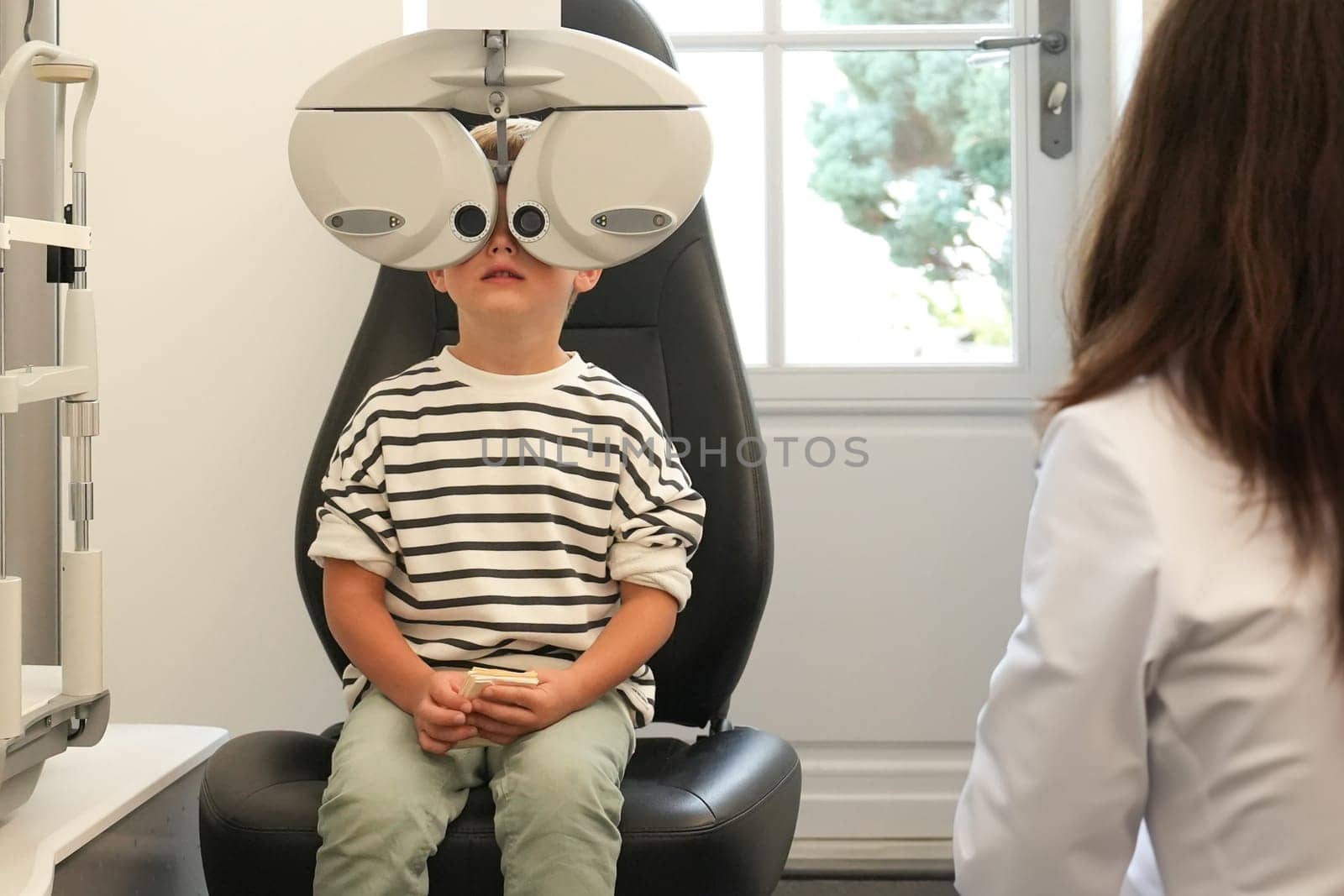 A little boy with ophthalmic equipment in clinic. Children's doctor examining