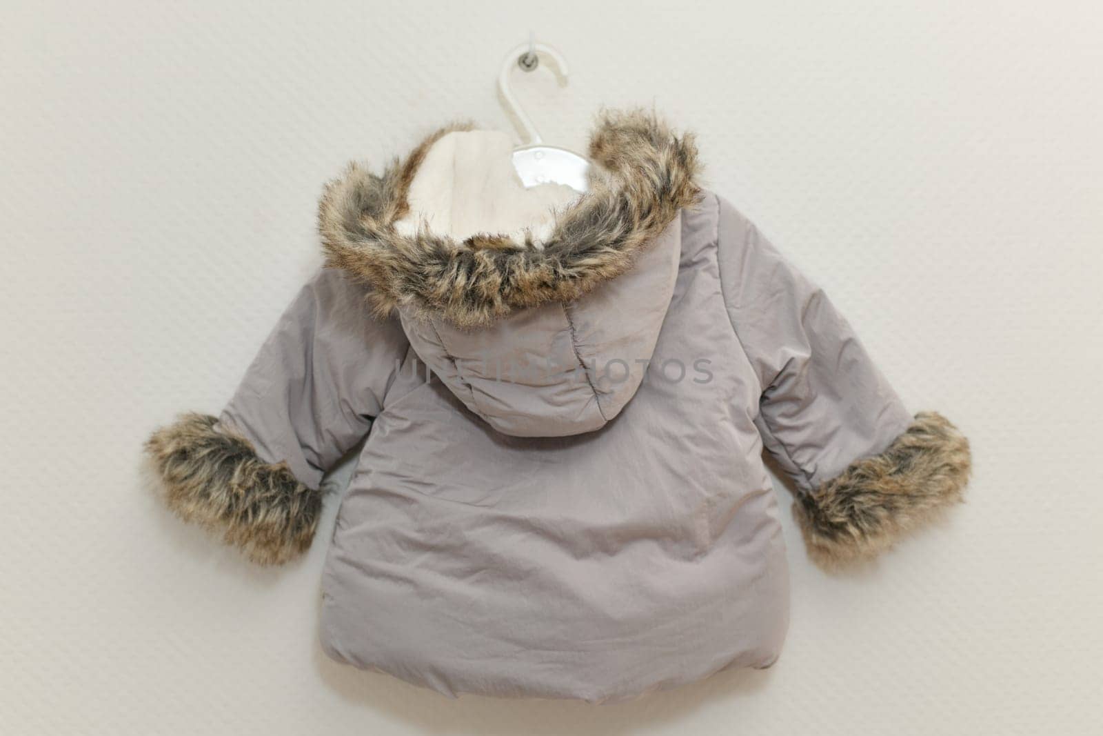 Grey-lilac colored fur jacket for girl hanging on hanger on white background