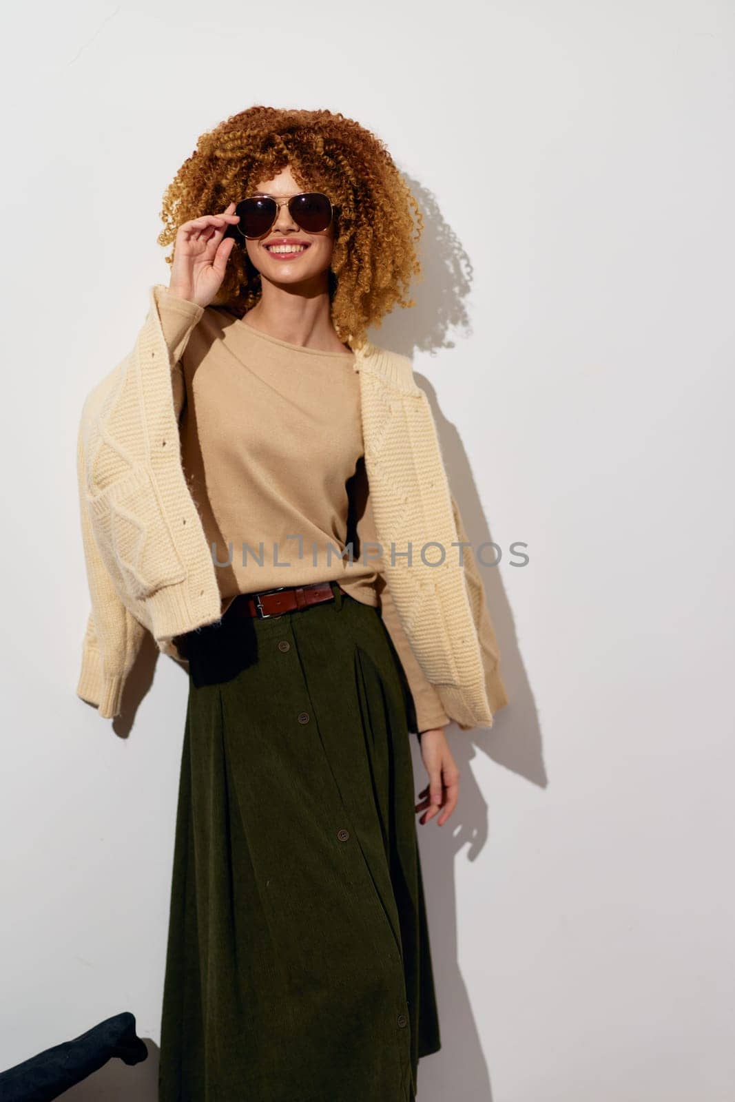 Chic young woman sporting a trendy outfit, including a beige top and olive green skirt, showcasing a confident pose against a bright white backdrop Perfect for fashion and style concepts