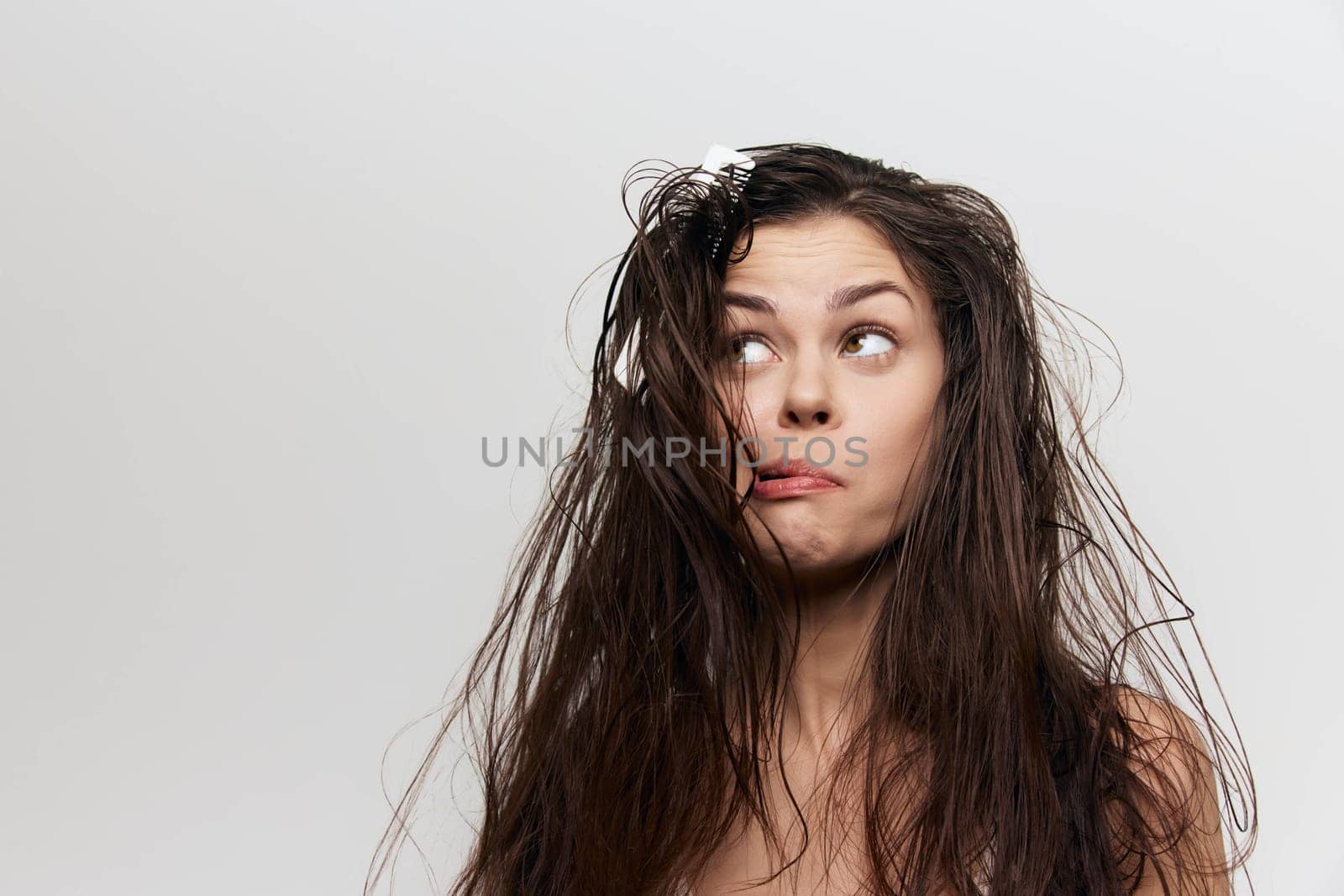 A young woman with unkempt hair appears playful and surprised, gazing upwards with a quirky expression The plain background emphasizes her unique hairstyle and vibrant personality