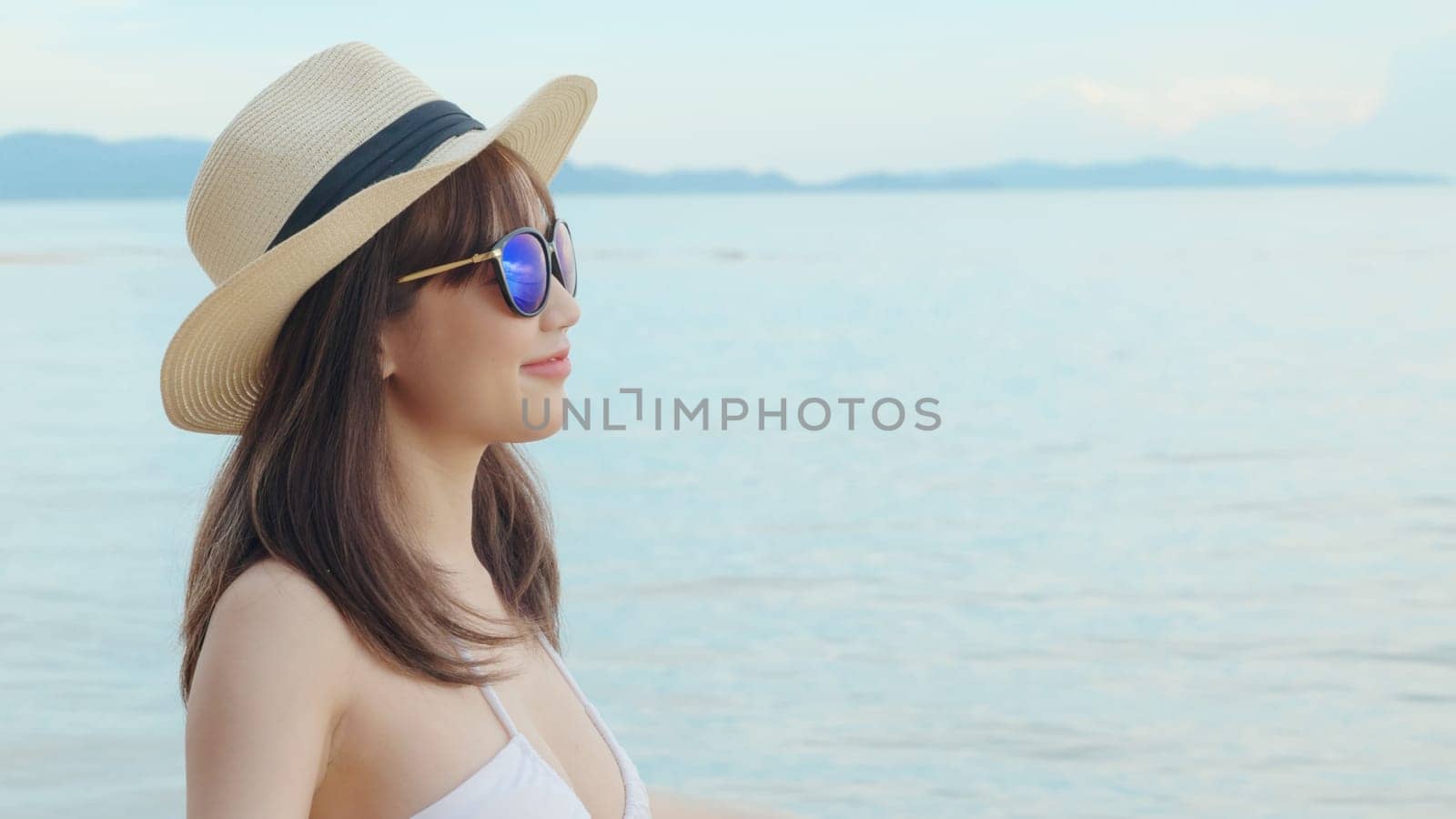 Beautiful Asian woman wearing hat and sunglasses at tropical paradise beach and smiling, Happy female in bikini swimsuit having fun eyewear in holidays summer vacation travel