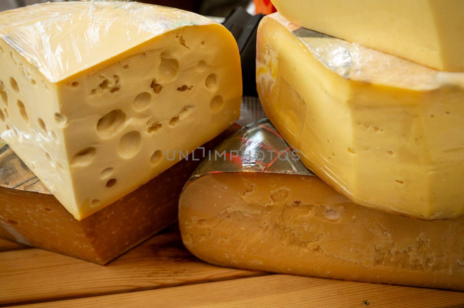 large circles of fresh cheese in section. Various types of cheese displayed at a market stall. Cheese blocks and slices arranged for sale at a farmers market