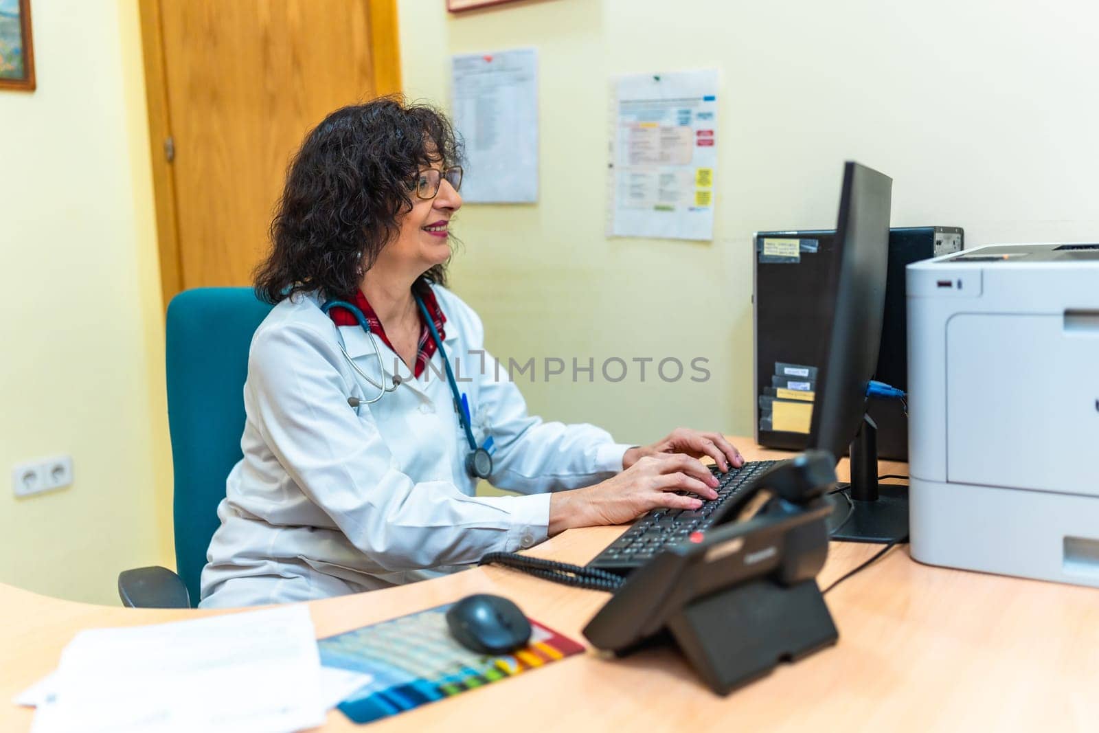 Senior female doctor typing on a desktop computer keyboard in her office at the nursing home