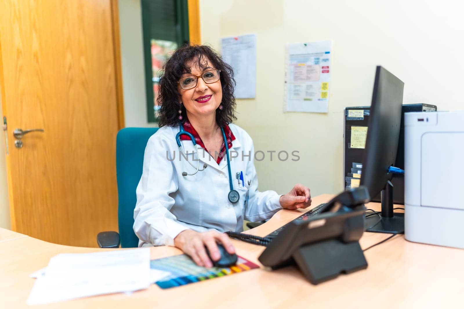 Senior female doctor using computer and managing patients' medical records in bright nursing home office
