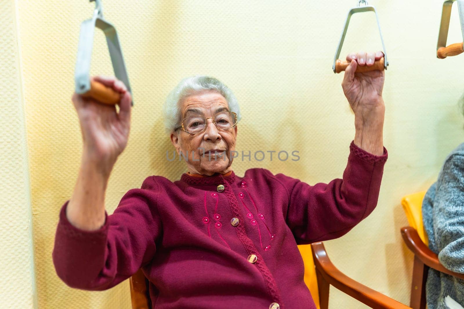 Senior woman performing physical therapy exercises with a pulley machine, promoting mobility and well being in a nursing home environment