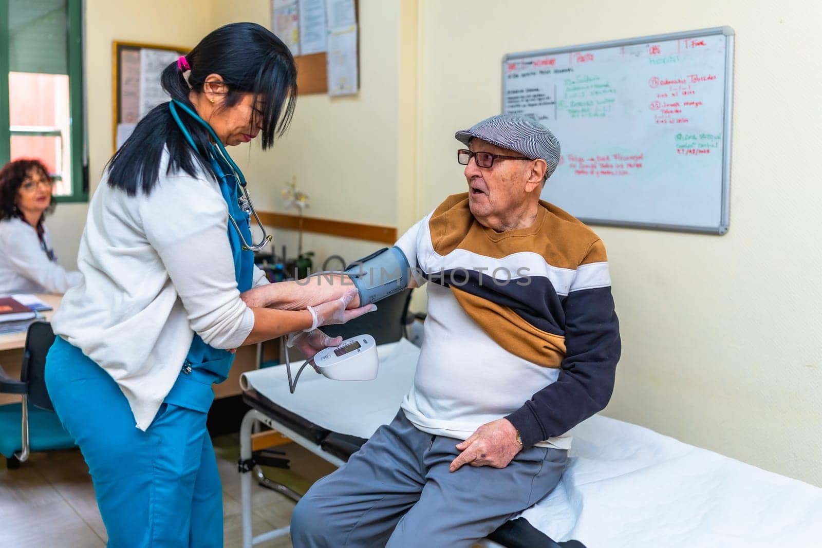 Female nurse checking blood pressure of elderly man sitting on examination table in medical clinic