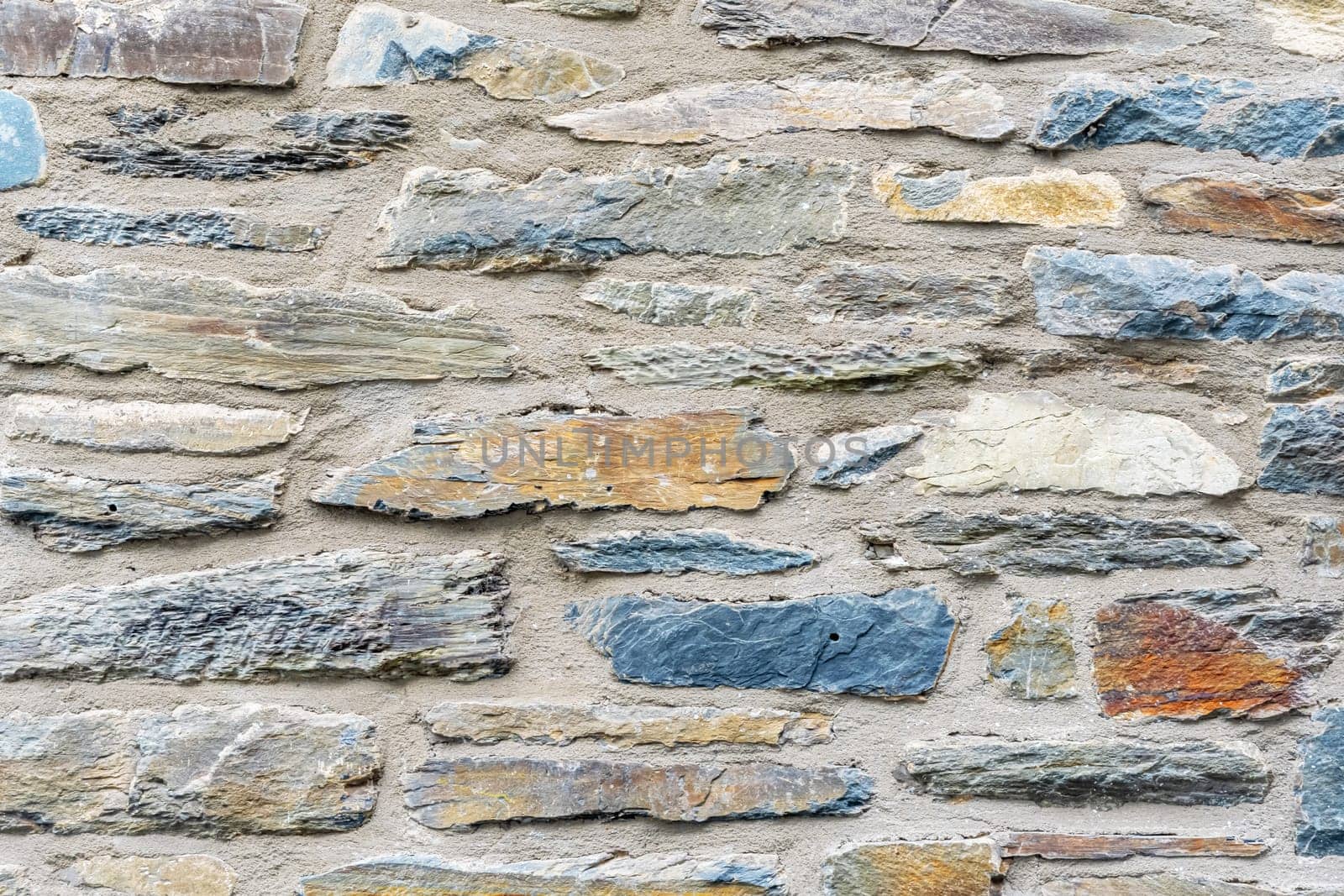 Close up view of old stone wall, ancient building methods showing textures and patterns of old stones and mortar, combination of grey, bluish and beige stones in masonry,